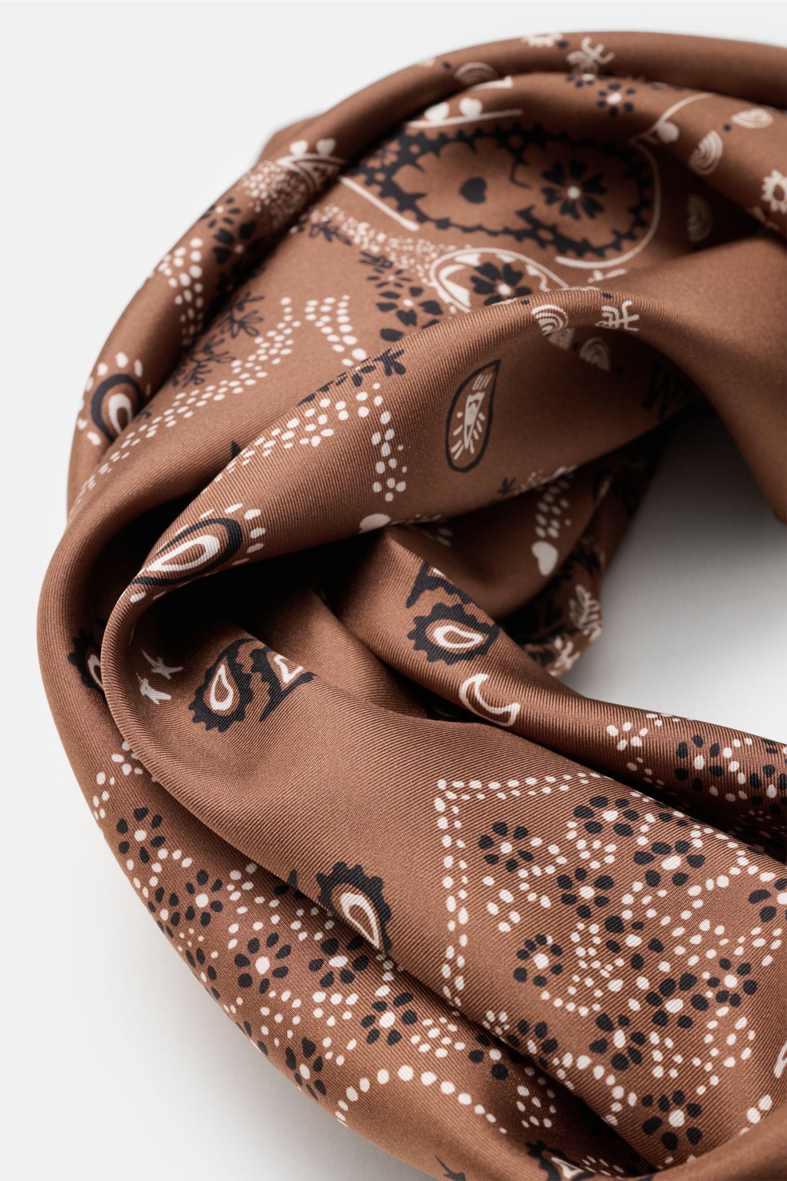 Close-up angled view of the Ace Denim Silk scarf brown/black/white patterned with paisley design on smooth pure silk fabric.

Eye-catching for the warm season: The ACE DENIM silk scarf in a bandana design is a casual statement accessory for summer look