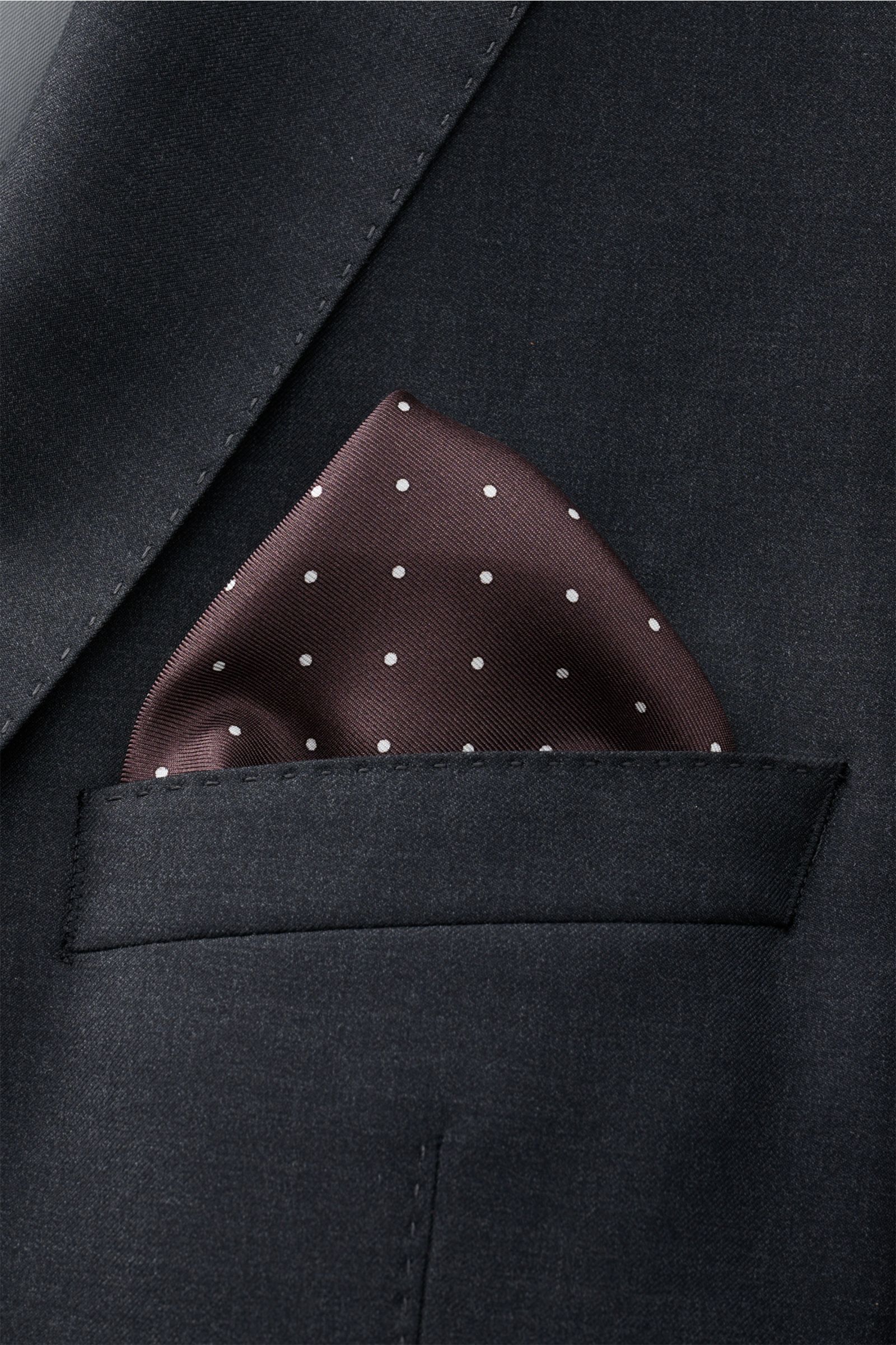 Close-up view of a Tom Ford Seiden-Einstecktuch dunkelbraun/weiß gepunktet pocket square in a dark suit pocket, showing its smooth silk texture and rolled edges.

Description: Dieses Einstecktuch von TOM FORD aus reiner Seide setzt mit seinem dezenten 