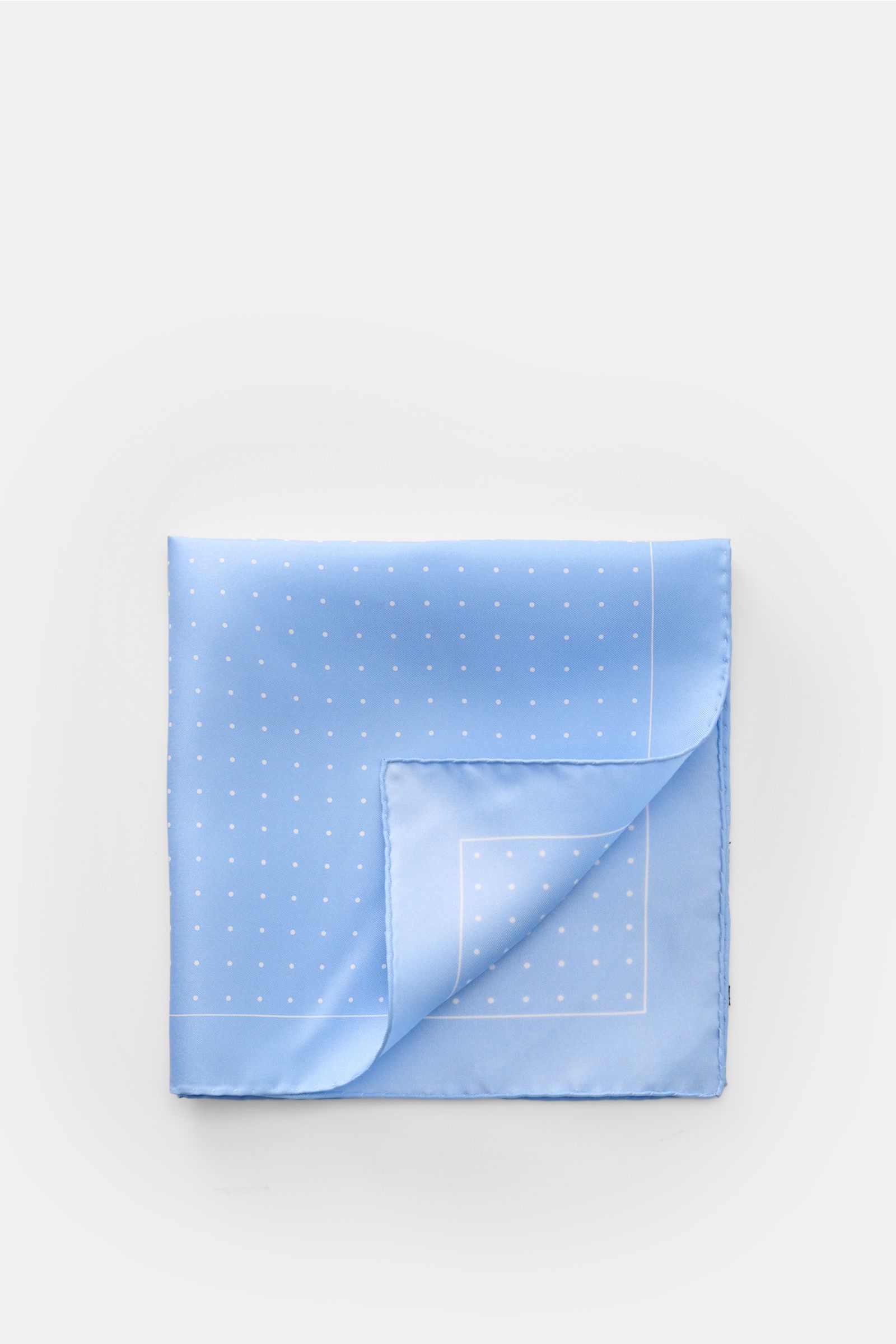 Top-down view of Tom Ford Seiden-Einstecktuch hellblau/weiß gepunktet, a light blue silk pocket square with white dots, rolled edges, and a subtle TOM FORD print, made in Italy, measuring approx. 40 cm x 40 cm. Dieses Einstecktuch von TOM FORD aus rein