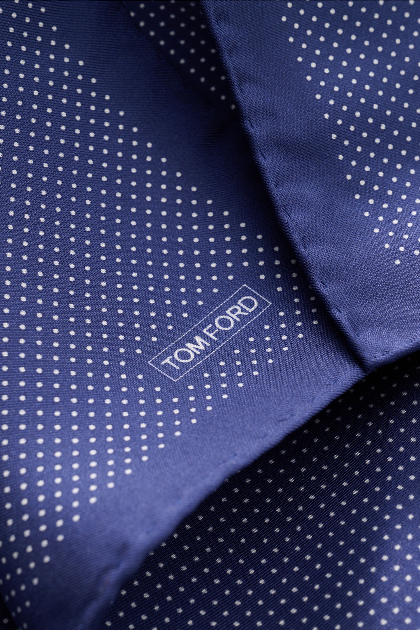Close-up shot of Tom Ford Seiden-Einstecktuch dunkelblau/weiß gepunktet, a navy silk pocket square with white polka dots, rolled edges, and a small TOM FORD logo print. Dieses Einstecktuch von TOM FORD aus reiner Seide setzt mit seinem dezenten Punktmu