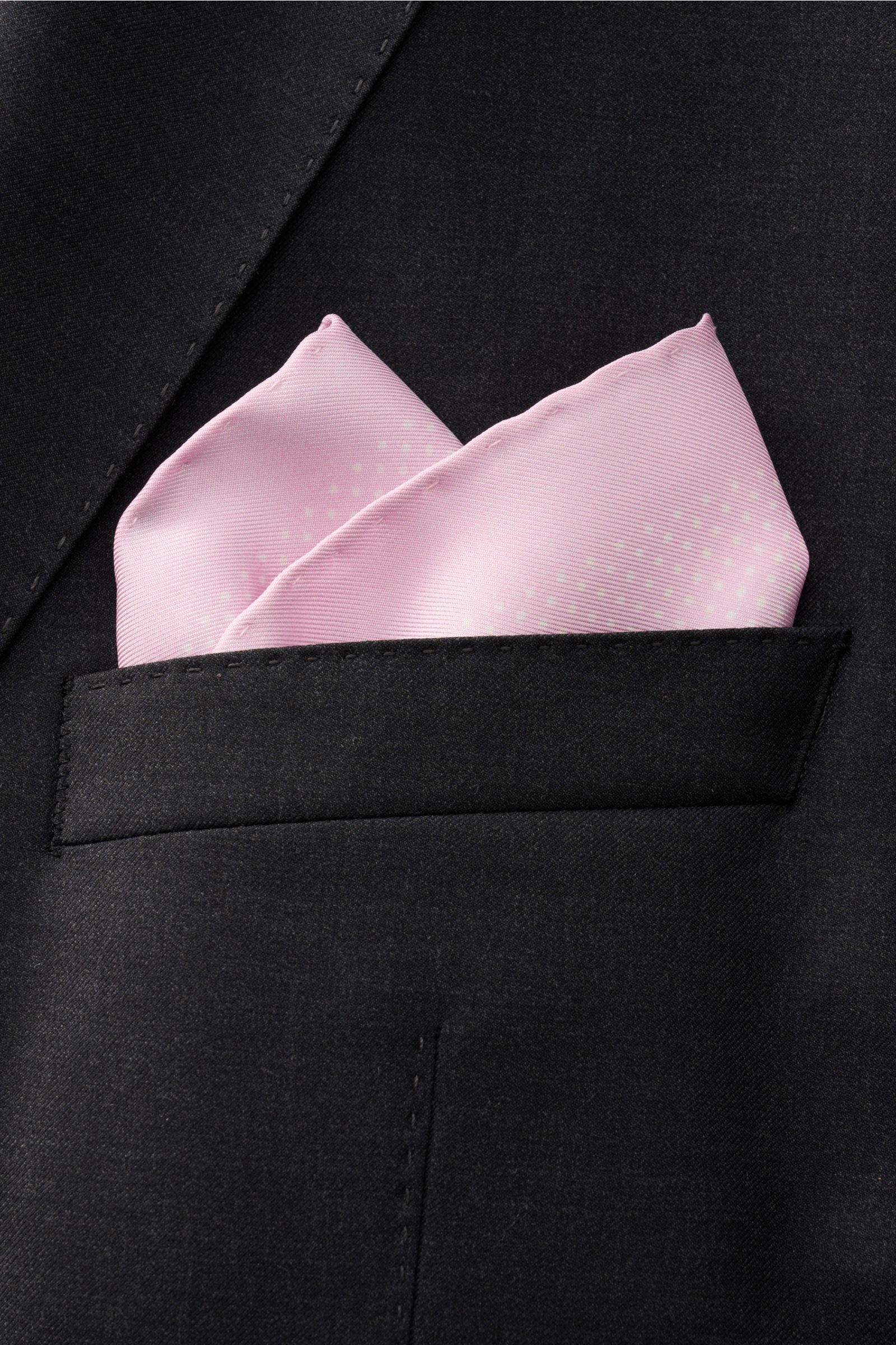 Close-up front view of a black jacket pocket featuring the Tom Ford Seiden-Einstecktuch rosé/weiß gepunktet, a pure silk pocket square with a subtle dot pattern, rolled edges, smooth feel, small TOM FORD print, made in Italy, approx. 39x39 cm.

Dieses 