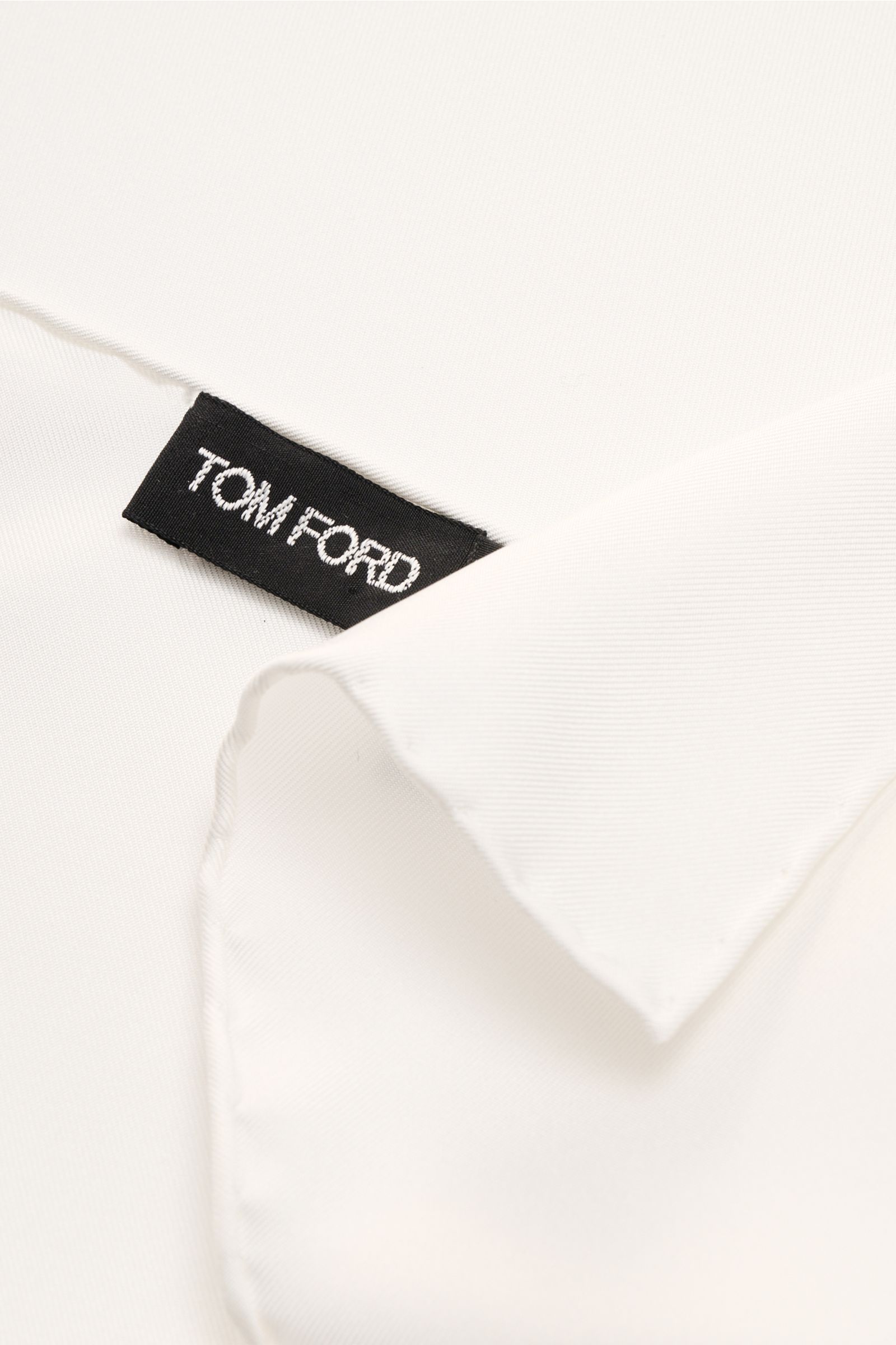 Close-up top-down view of the Tom Ford Silk pocket square white showing smooth pure silk fabric, rolled edges, and a black Tom Ford label.

Description: 
A detail that makes all the difference: This exclusive pocket square by TOM FORD in pure silk with