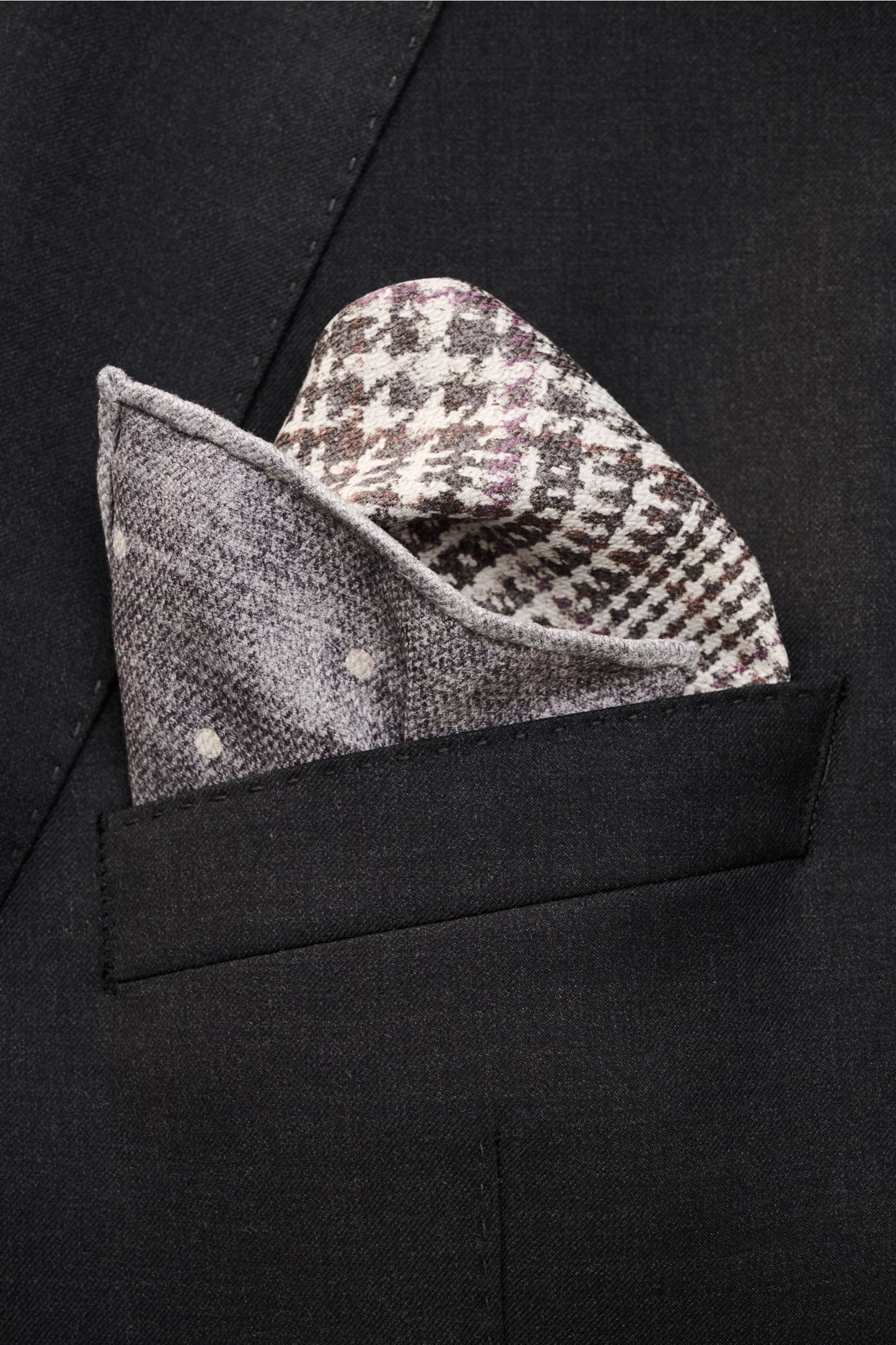 Close-up front view of a Brunello Cucinelli Seiden-Einstecktuch dunkelgrau/off-white gemustert in a black jacket pocket, featuring reine Seide, geschmeidiger Griff, Glencheck pattern, Punkte auf der Rückseite, handrollierte Kanten, Made in Italy, Maße: ca