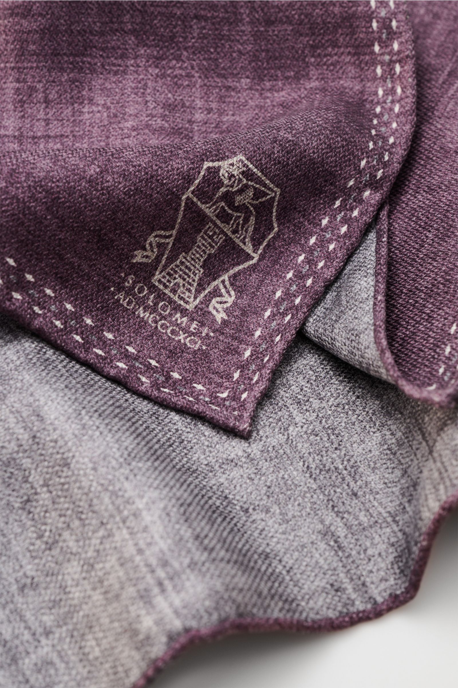 Close-up image from a top-side angle of the Brunello Cucinelli Seiden-Einstecktuch violett/grau meliert, showing folded fabric with a subtle logo, featuring reine Seide, geschmeidiger Griff, handrollierte Kanten, Made in Italy, Maße: ca. 35 cm x 35 cm.