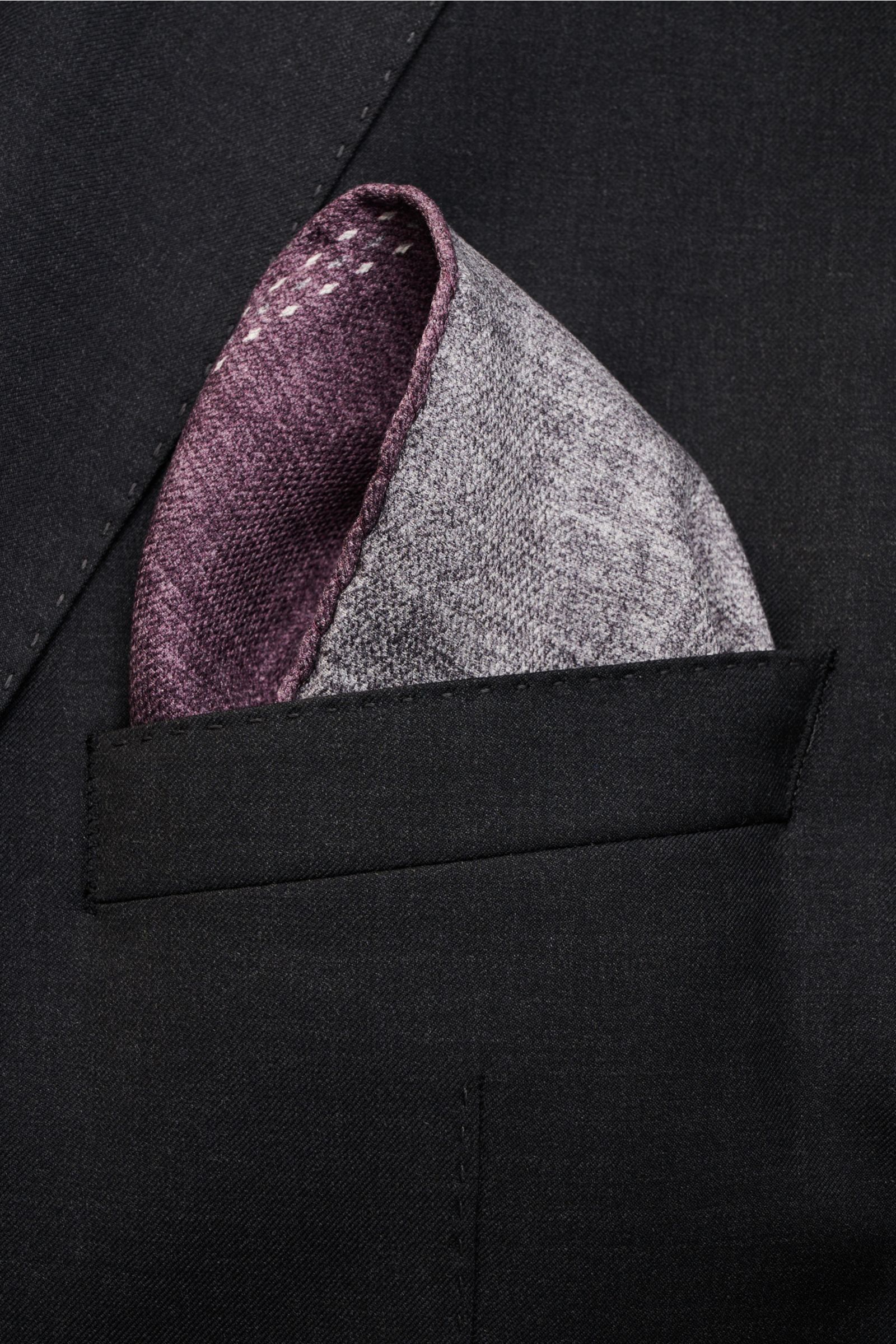 Close-up front perspective of a Brunello Cucinelli Seiden-Einstecktuch violett/grau meliert in a black jacket pocket, showing its pure silk, smooth touch, hand-rolled edges, Made in Italy, approx. 35 cm x 35 cm.