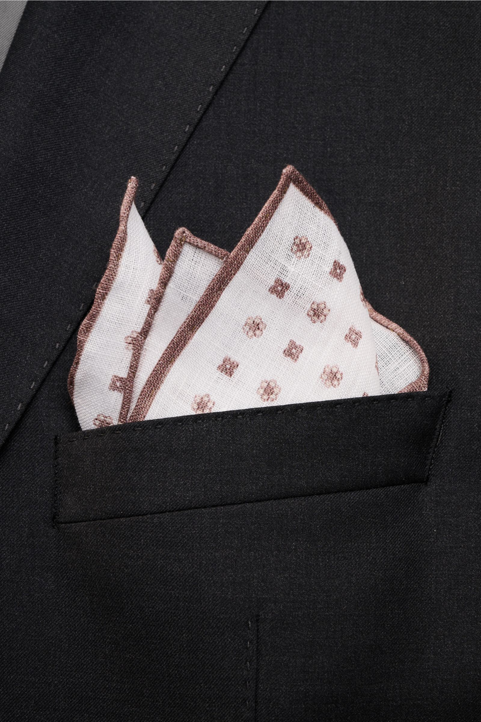 Rosi Collection Linen pocket square 'Fox' white/brown patterned in black jacket pocket, photographed from front close-up. Pure linen, soft feel, floral print, rolled edges, made in Italy, dimensions: 31.5 cm x 31.5 cm.