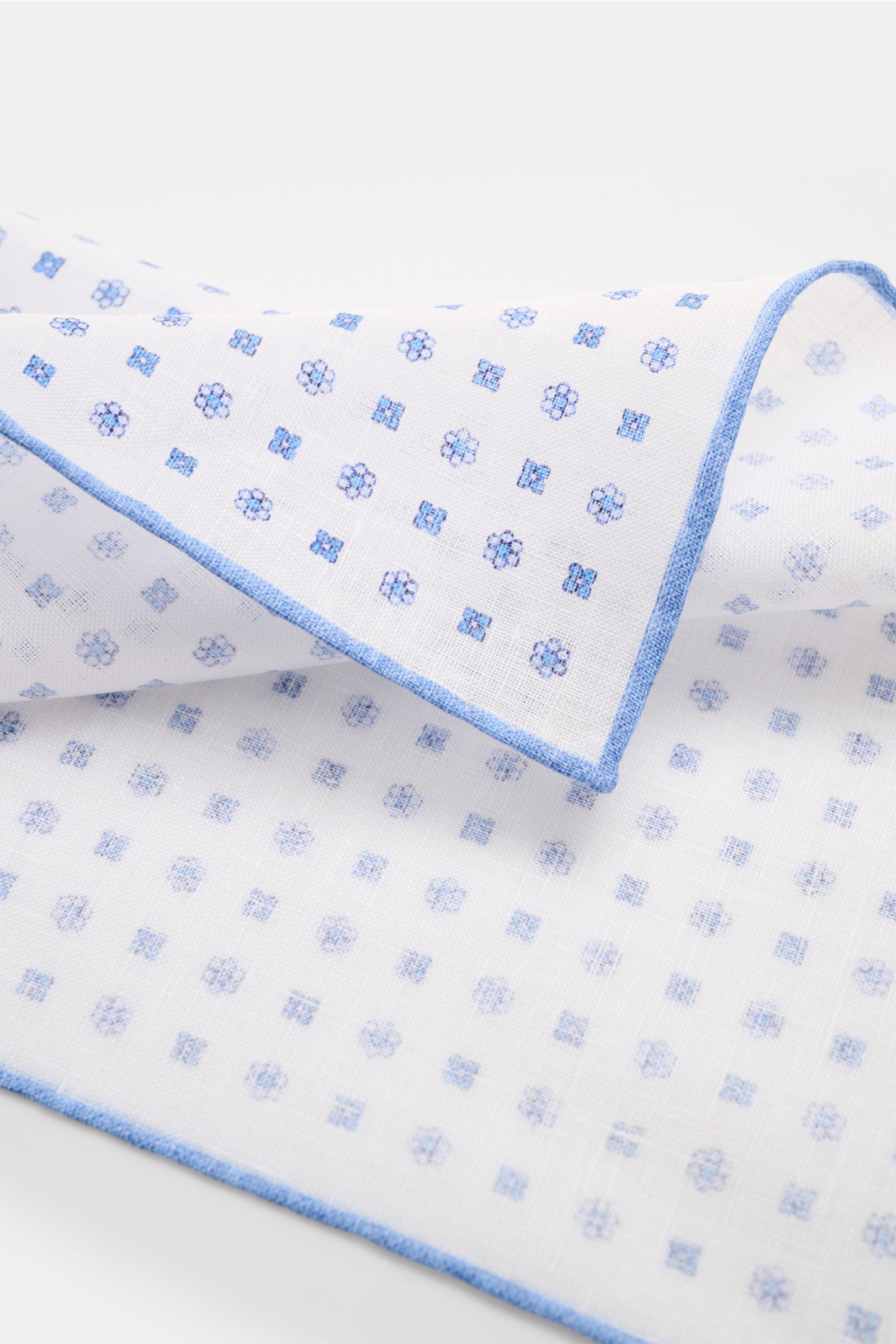 Rosi Collection Linen pocket square 'Fox' white/blue patterned shown from a close-up angled top view, pure linen, soft feel, floral print, rolled edges, made in Italy, dimensions 31.5 cm x 31.5 cm.