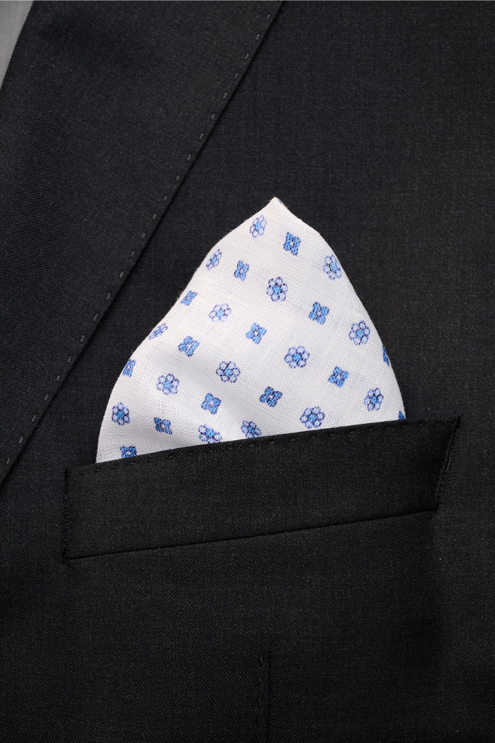Rosi Collection Linen pocket square 'Fox' white/blue patterned shown from front close-up in a black jacket pocket, pure linen, soft feel, floral print, rolled edges, made in Italy, dimensions 31.5 cm x 31.5 cm.