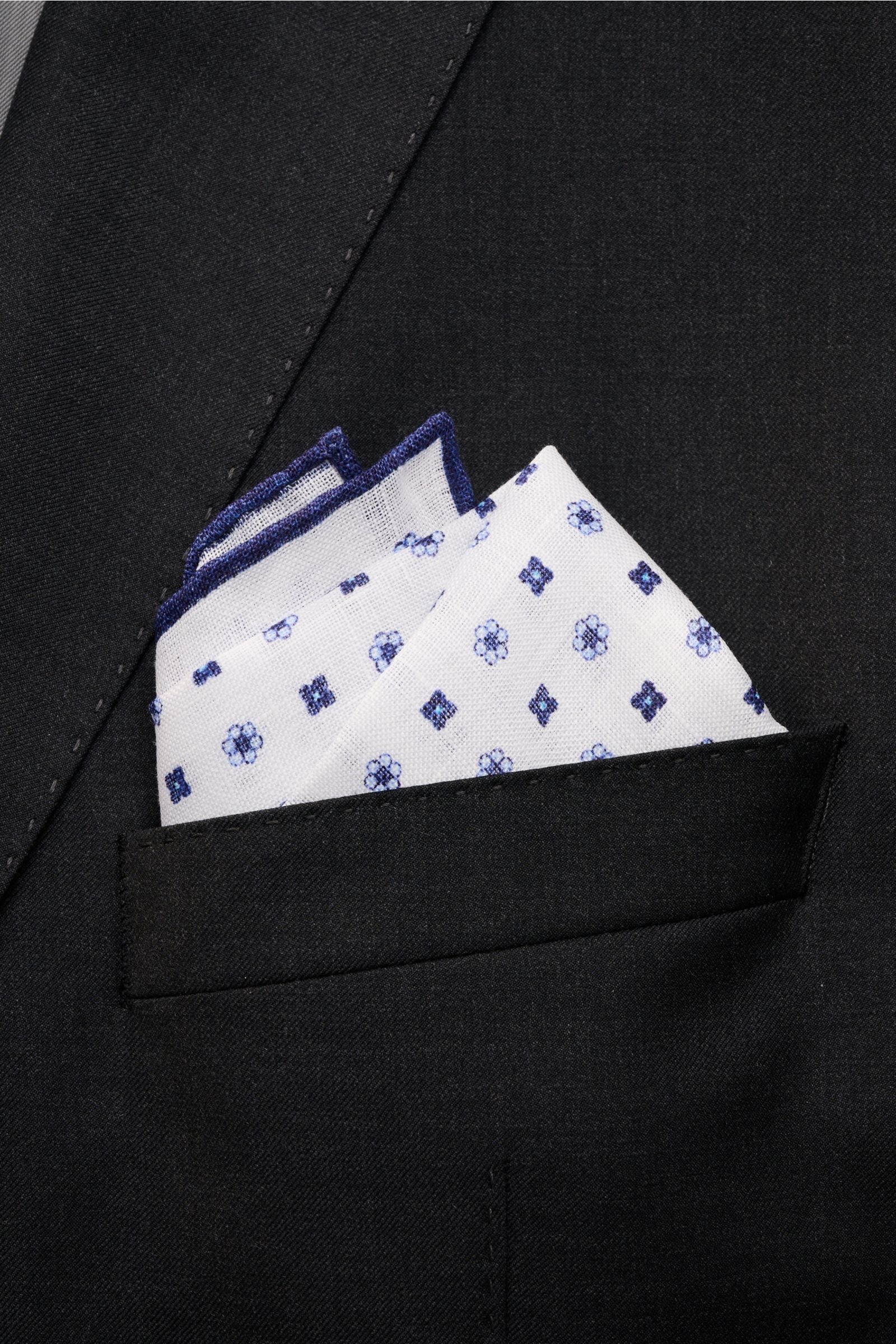 Rosi Collection Linen pocket square 'Fox' white/navy patterned in black jacket pocket, pure linen, soft feel, floral print, rolled edges, made in Italy, 31.5 x 31.5 cm, close-up front view.