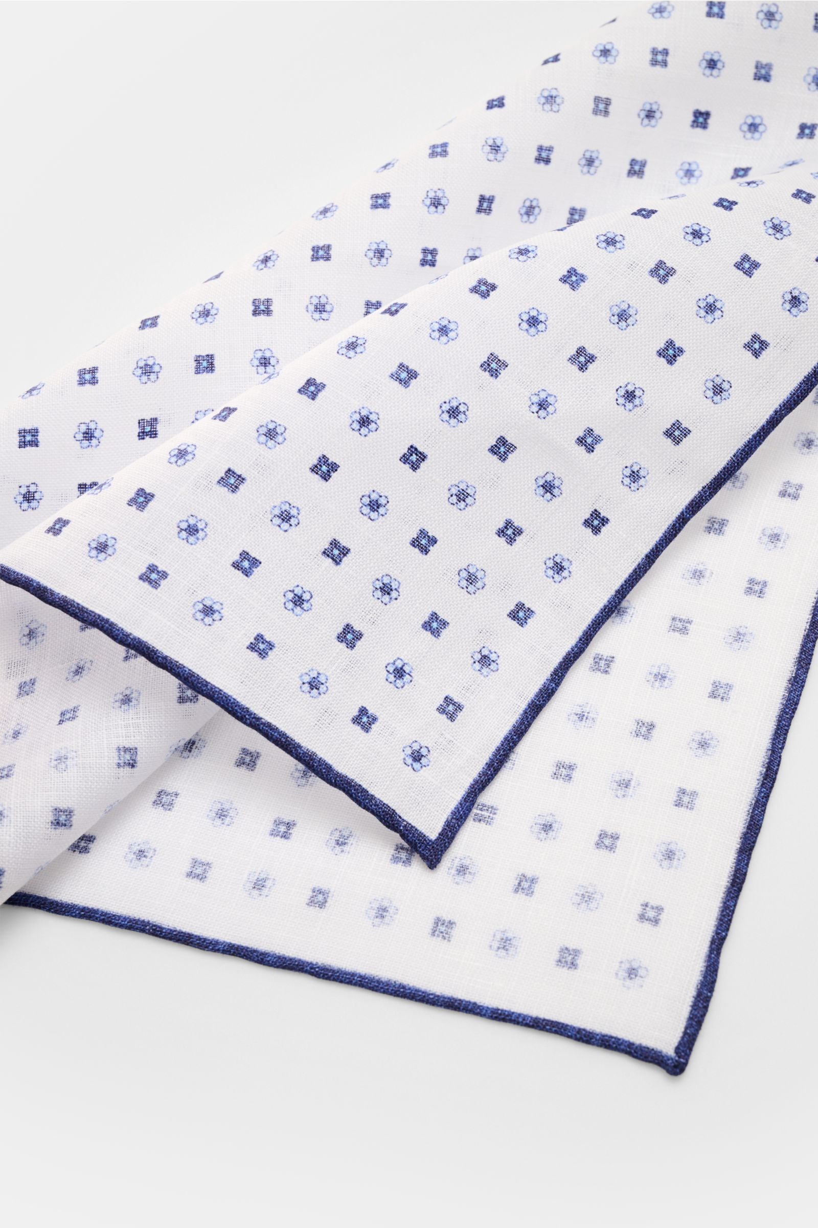 Rosi Collection Linen pocket square 'Fox' white/navy patterned shown from a folded top angle, pure linen, soft feel, floral print, rolled edges, made in Italy, dimensions 31.5 cm x 31.5 cm.