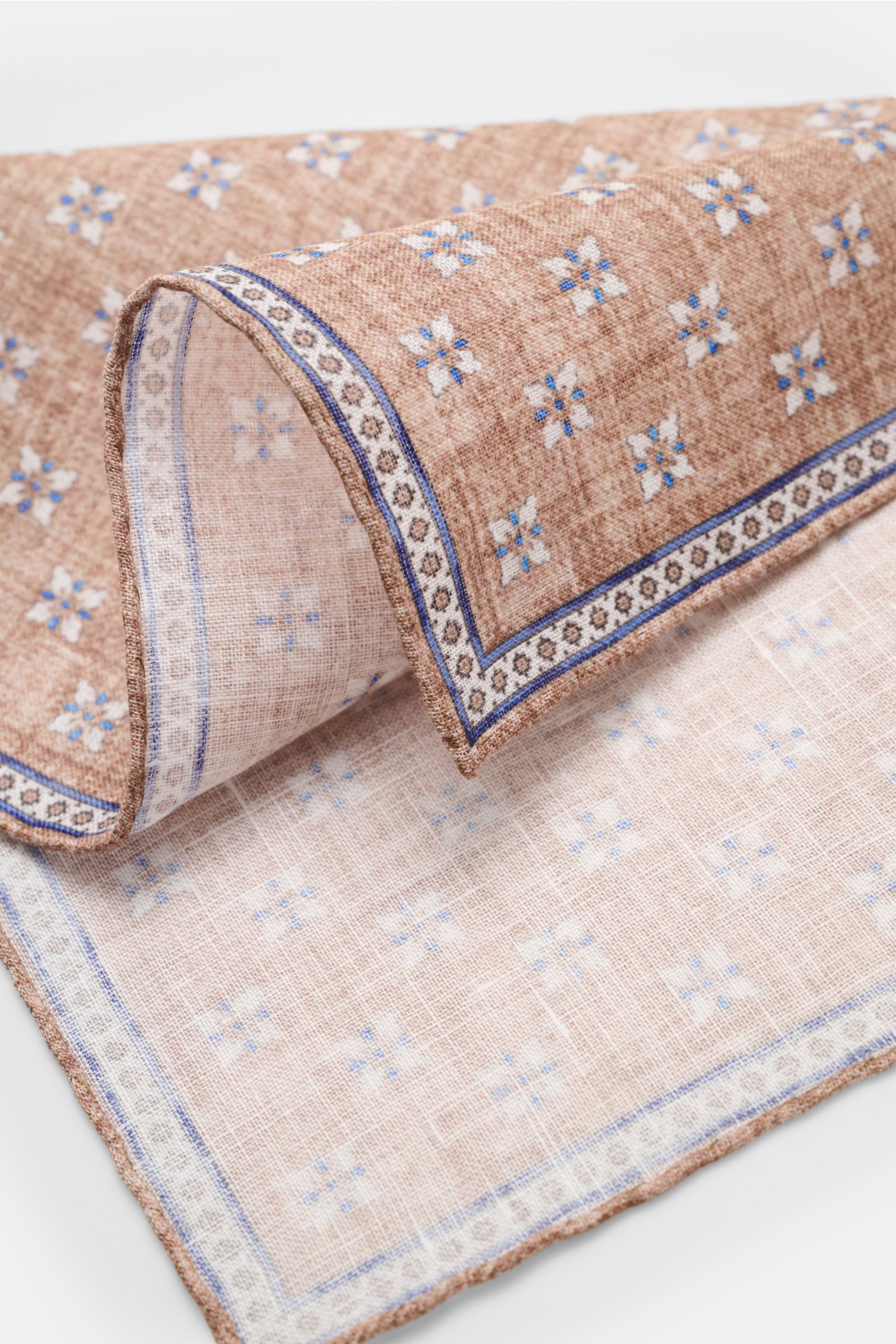 Rosi Collection Linen pocket square 'Fox' light brown/blue/off-white patterned, pure linen, soft feel, floral print with edging, rolled edges, made in Italy, 31x31 cm, shown from close-up side angle.