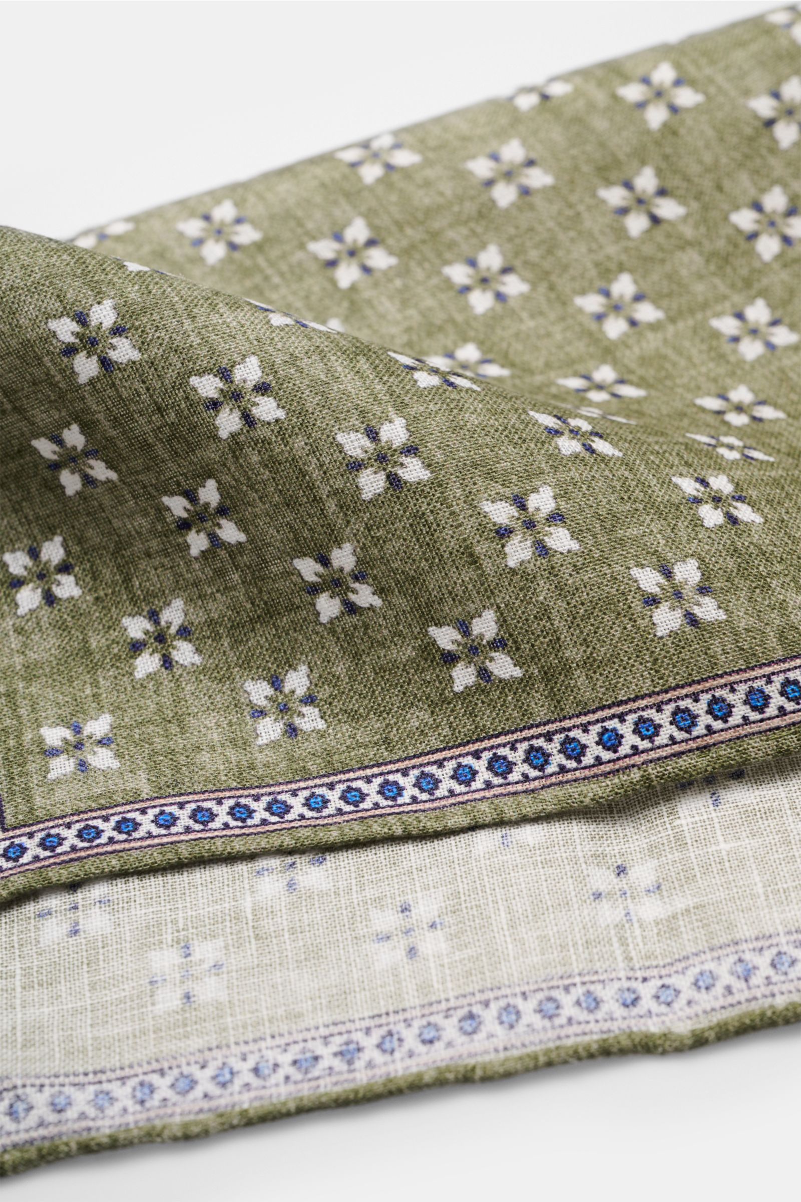 Close-up angled view of the Rosi Collection Linen pocket square 'Fox' olive/dark blue/white patterned, pure linen, soft feel, floral print with edging, rolled edges, made in Italy, dimensions 31 cm x 31 cm.