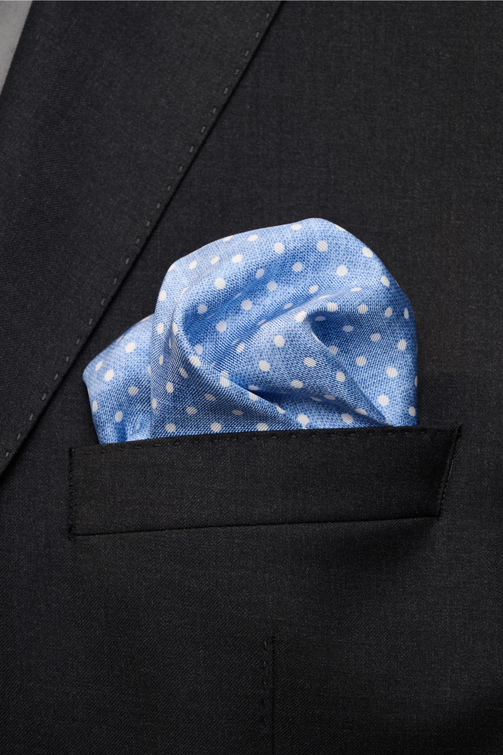 Rosi Collection Seiden-Einstecktuch 'Silk' hellblau/weiß gepunktet, aus reiner Seide mit softem Griff, rollierten Kanten, ca. 31x31 cm, Made in Italy, in schwarzer Jackettasche, frontal fotografiert.