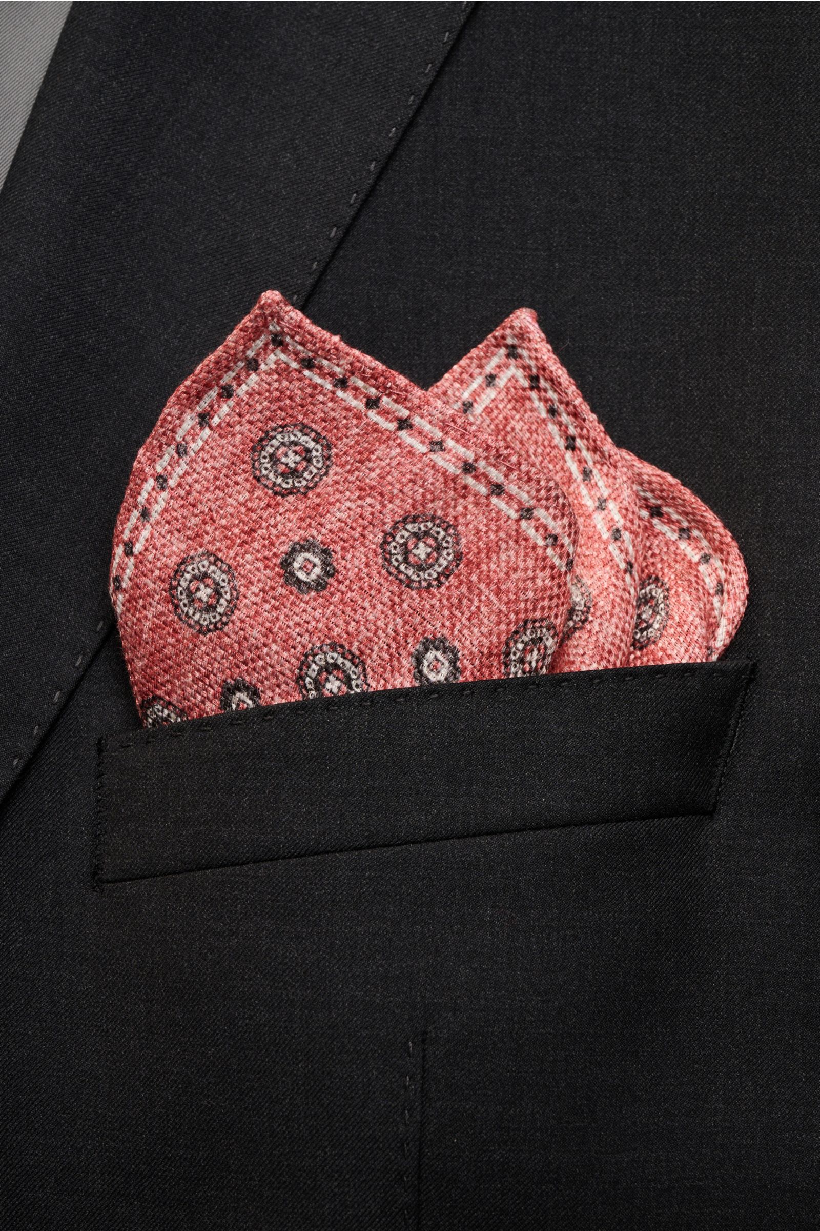 Nahaufnahme des Rosi Collection Einstecktuchs 'Joy' hellrot/weiß/schwarz gemustert mit floralem Retro-Muster, aus Seide und Leinen, in schwarzer Sakko-Brusttasche, von vorne fotografiert.