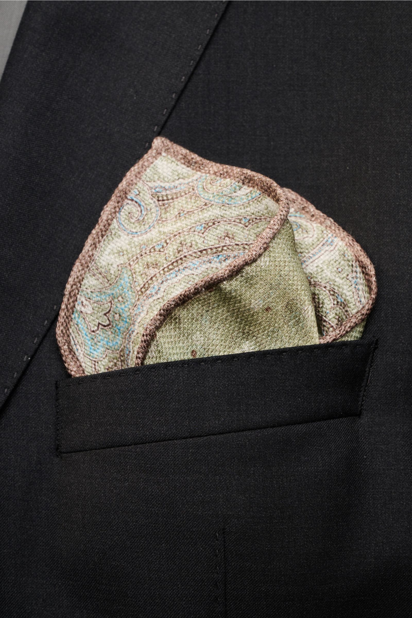 Alt tag (125 characters max):  
Front close-up of Rosi Collection Einstecktuch 'Joy' salbei/hellblau/braun gemustert in a black jacket pocket with paisley pattern.

Additional description:  
Eleganter Eyecatcher: Mit seinem modernen Paisley-Muster wird