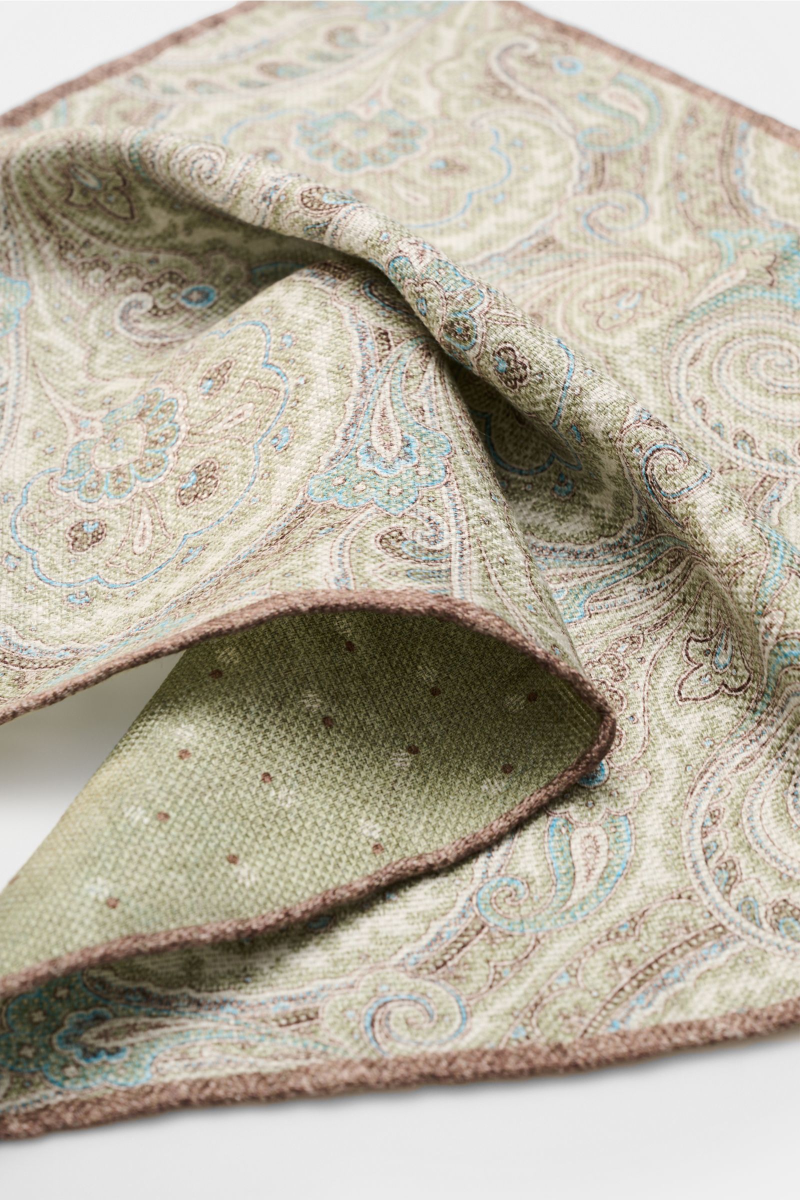 Close-up angled view of Rosi Collection Einstecktuch 'Joy' salbei/hellblau/braun gemustert with paisley pattern, silk-linen mix, rolled edges.

Eleganter Eyecatcher: Mit seinem modernen Paisley-Muster wird das Einstecktuch von ROSI COLLECTION zum hochw