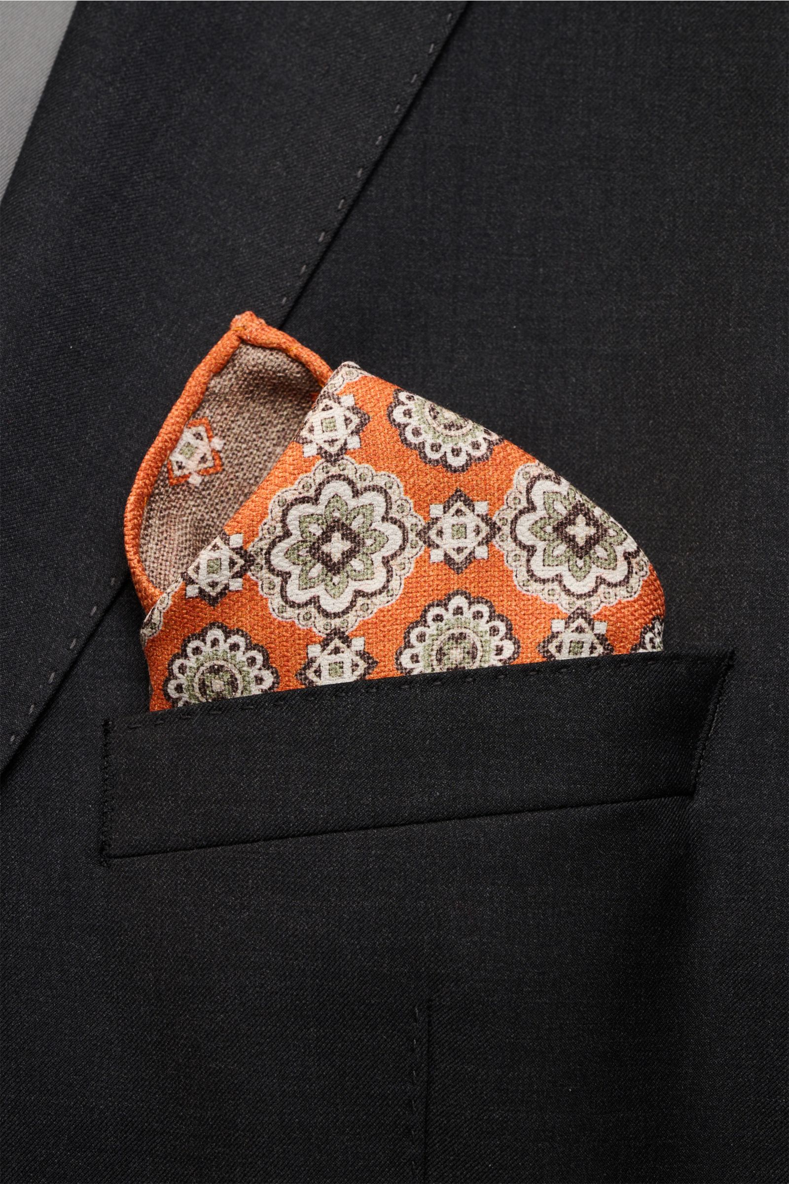Close-up front view of a black suit jacket pocket featuring the Rosi Collection Seiden-Einstecktuch 'Easy' orange/braun/salbei gemustert pocket square, made of reine Seide, softer, geschmeidiger Griff, elegant Medaillon-Print mit Borte, kontrastierende Rü