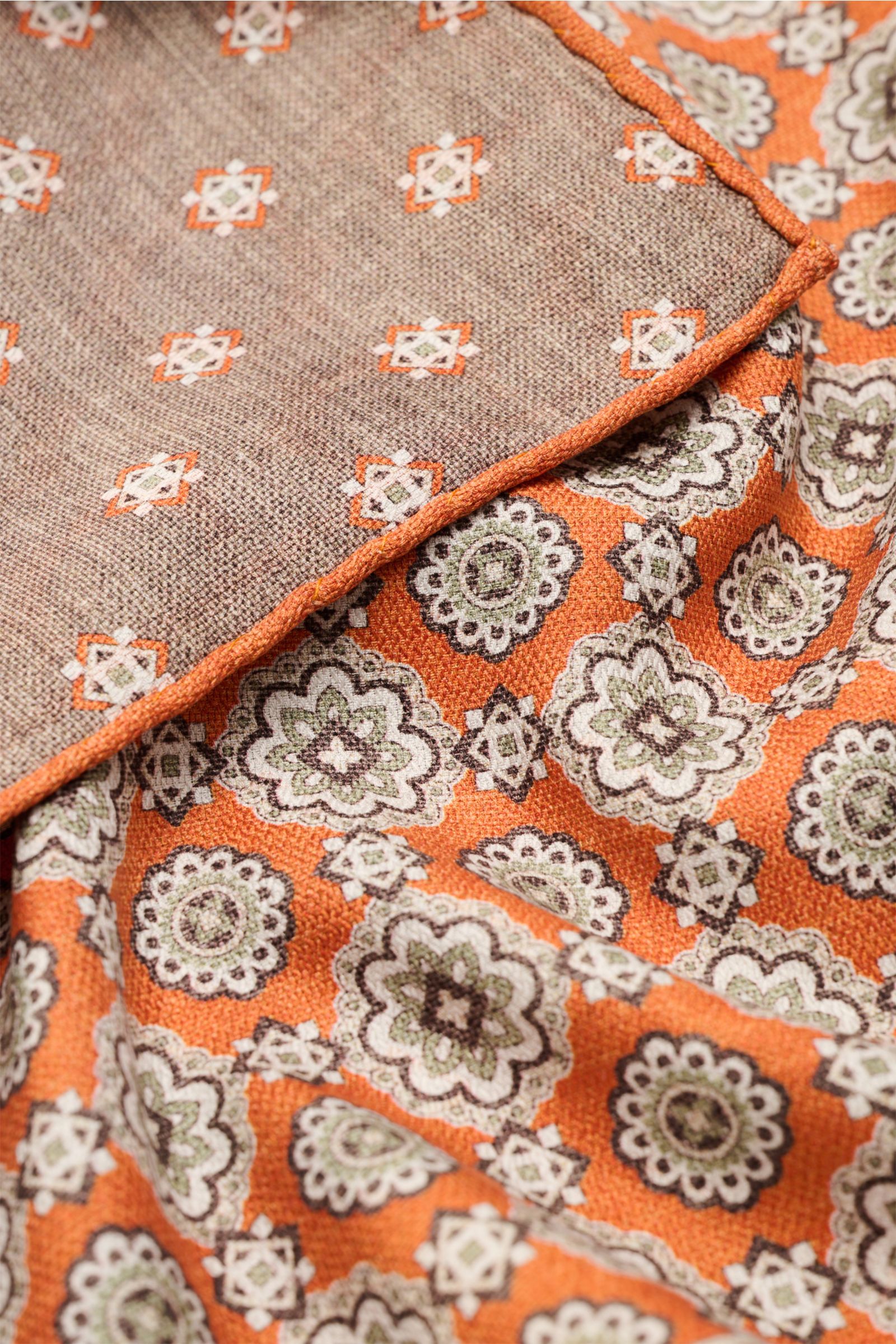 Close-up angled view of the Rosi Collection Seiden-Einstecktuch 'Easy' orange/braun/salbei gemustert showing its elegant medallion-print with border, contrasting back, rolled edges, made of pure silk with a soft, smooth feel, made in Italy, dimensions app