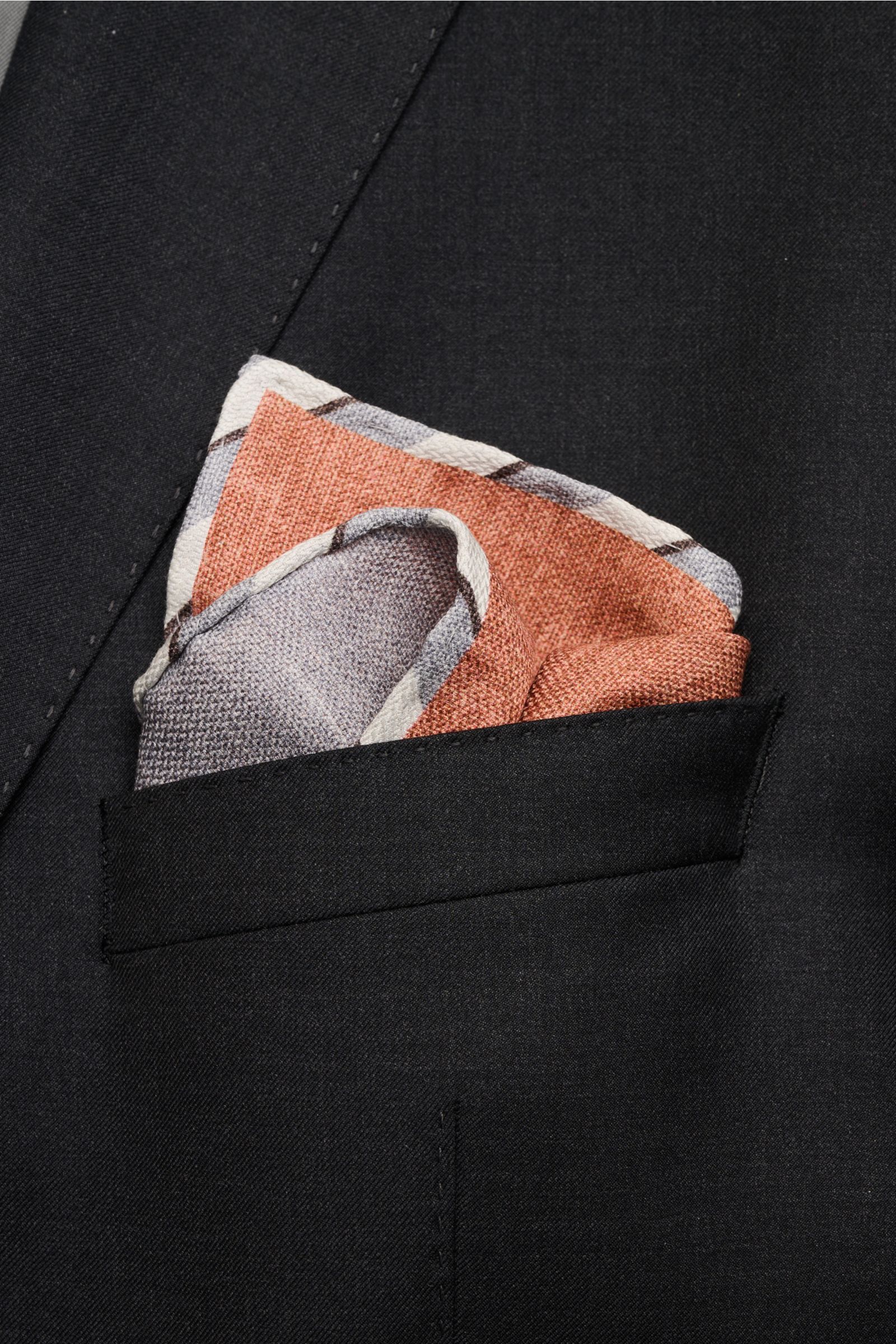 Brunello Cucinelli Seiden-Einstecktuch braun/grau meliert folded in a black suit pocket, photographed from a close-up front angle.

Quiet Luxury kann BRUNELLO CUCINELLI besonders gut und bringt auch in dieser Saison passende Einstecktücher, wie dieses 