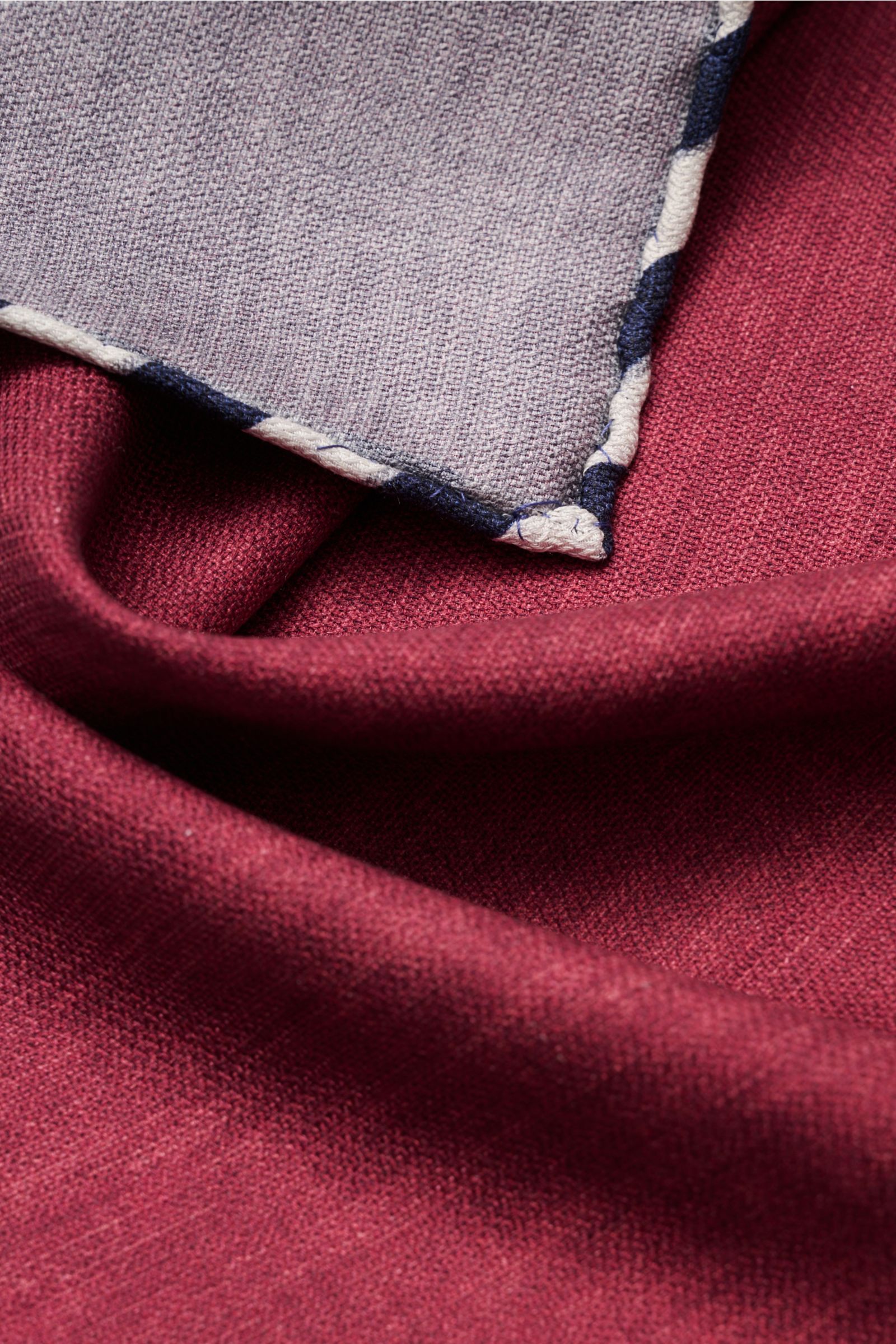 Brunello Cucinelli Seiden-Einstecktuch bordeaux/graublau meliert shown close-up from above, highlighting fabric texture and hand-rolled edges. Quiet Luxury kann BRUNELLO CUCINELLI besonders gut und bringt auch in dieser Saison passende Einstecktücher, wie