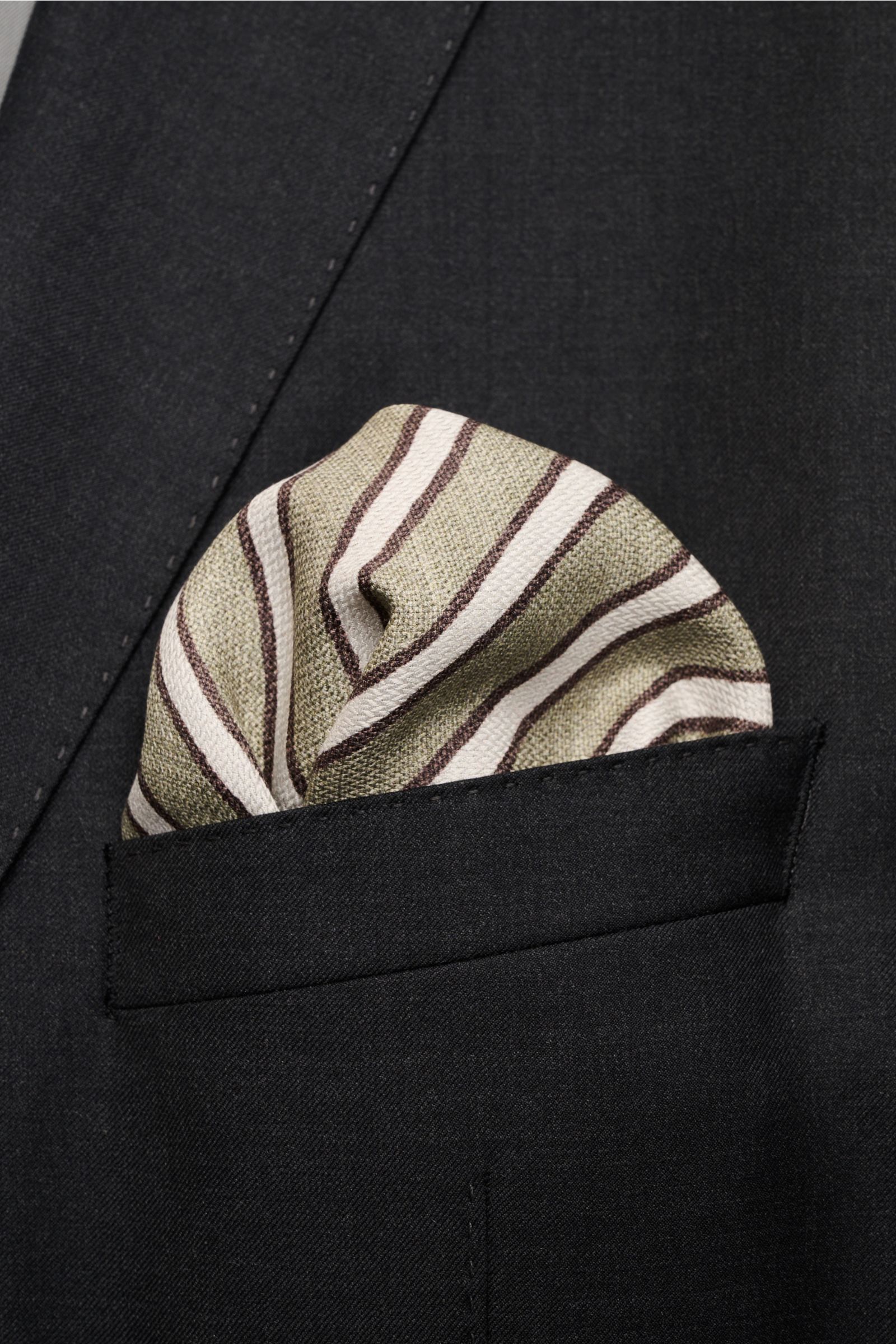 Brunello Cucinelli Seiden-Einstecktuch graugrün/hellgrau/dunkelbraun gestreift, handrollierte Kanten, aus leichter Vogelperspektive in dunkler Sakko-Brusttasche.