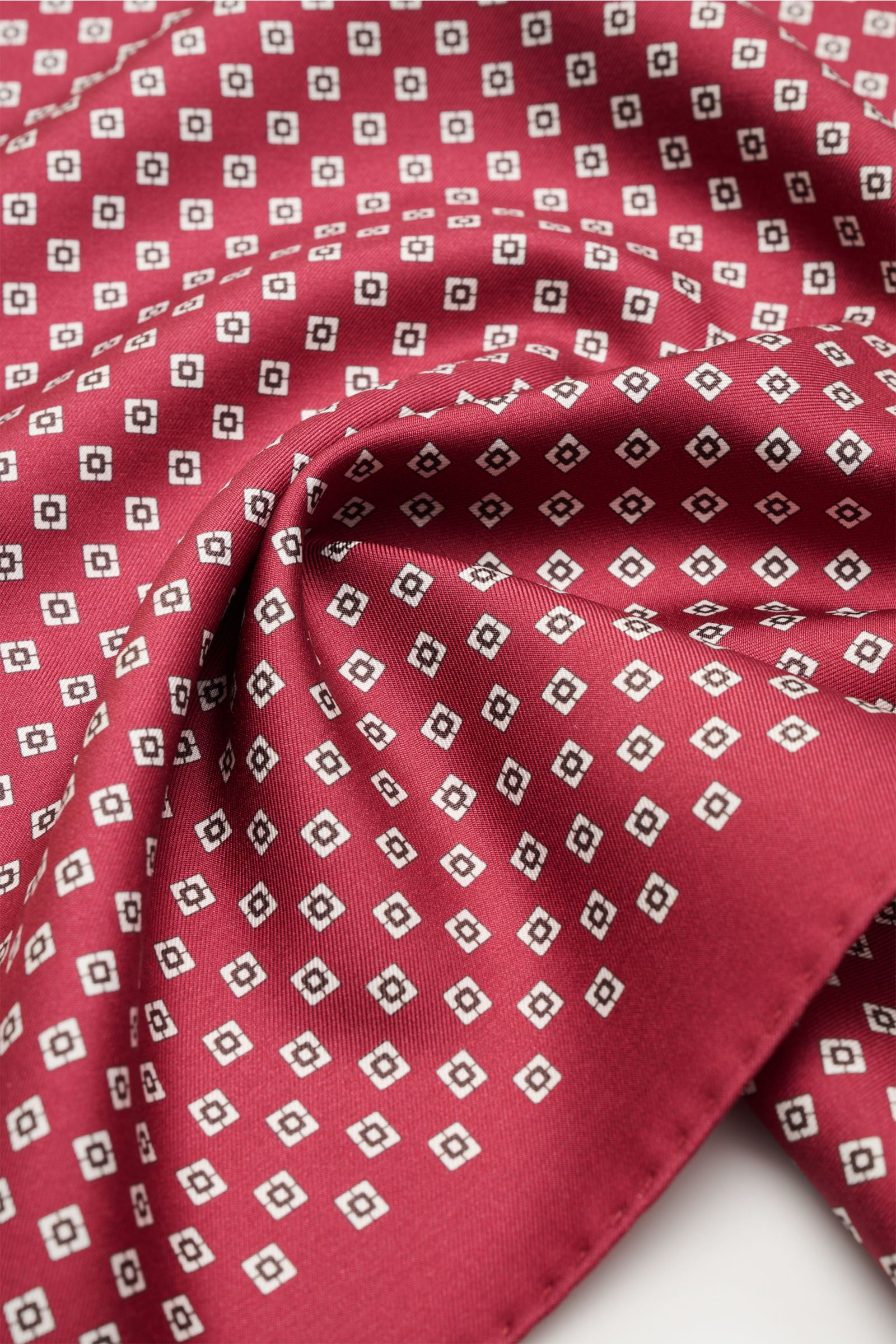 Close-up, angled top view of the Brunello Cucinelli Seiden-Einstecktuch dunkelrot/hellgrau/navy gestreift showing its smooth silk fabric with a subtle striped pattern and hand-rolled edges.

Description: Quiet Luxury heißt der große Trend: Das kann BRU