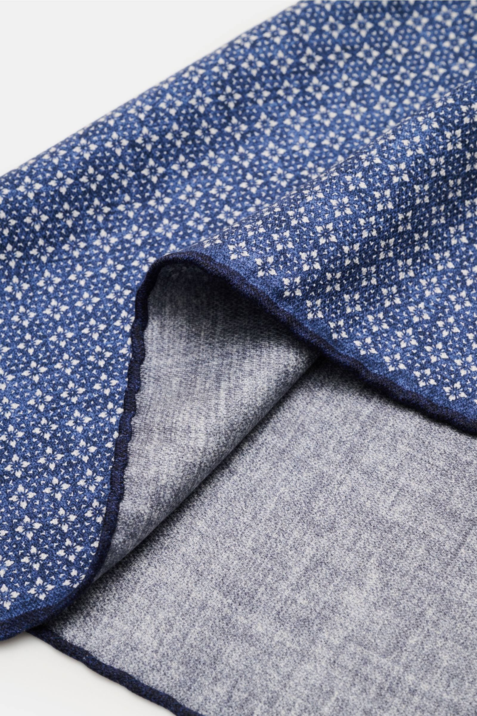 Brunello Cucinelli Seiden-Einstecktuch dunkelblau/grau gemustert shown from a close-up angle, folded to reveal floral pattern, handrolled edges, and smooth silk texture. Quiet Luxury heißt der große Trend: Das kann BRUNELLO CUCINELLI besonders gut und 