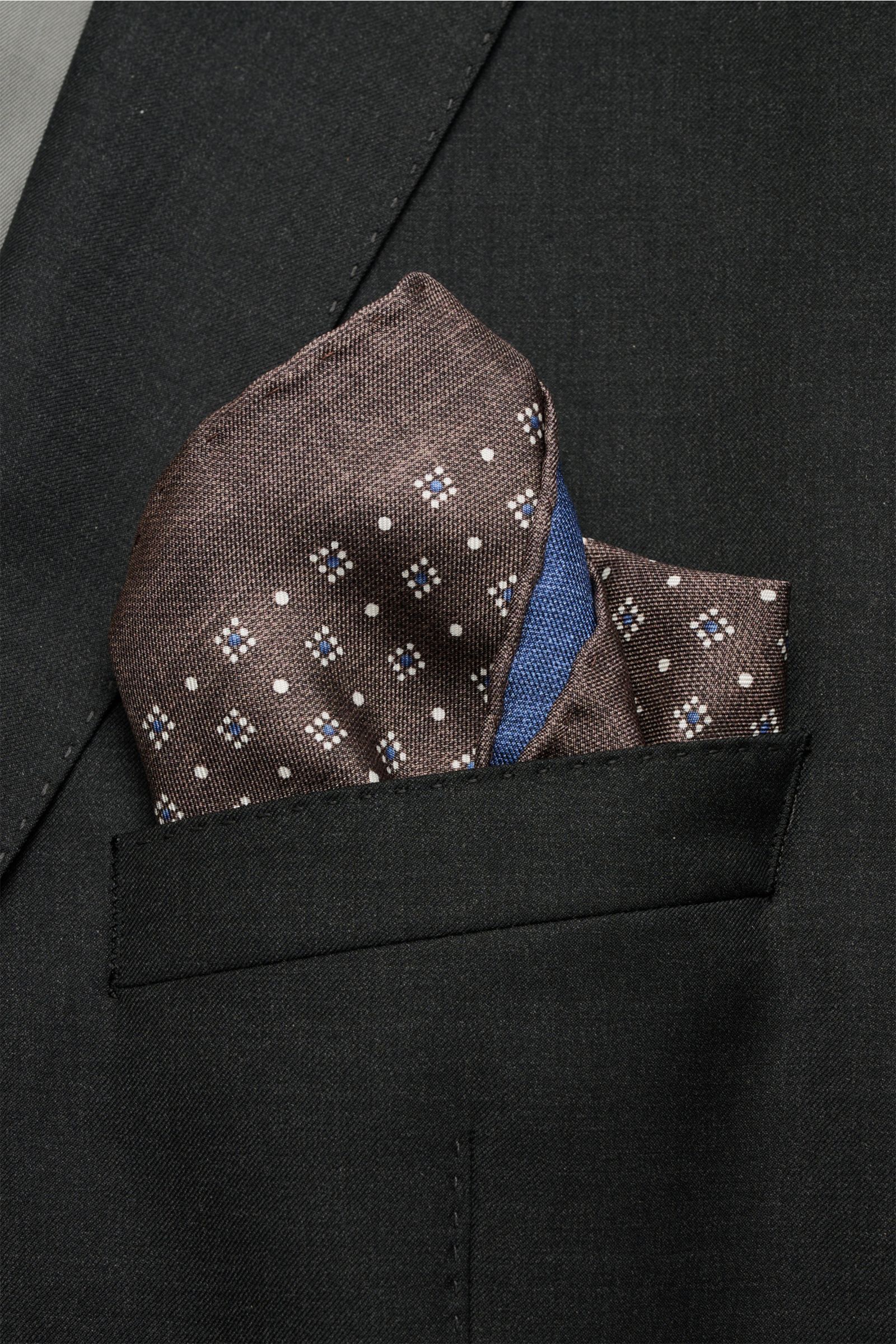 Close-up front view of a Brunello Cucinelli Seiden-Einstecktuch dunkelblau/graubraun/weiß gemustert pocket square in a black jacket pocket, featuring a graphic pattern.

Quiet Luxury kann BRUNELLO CUCINELLI besonders gut und bringt auch in dieser Saiso