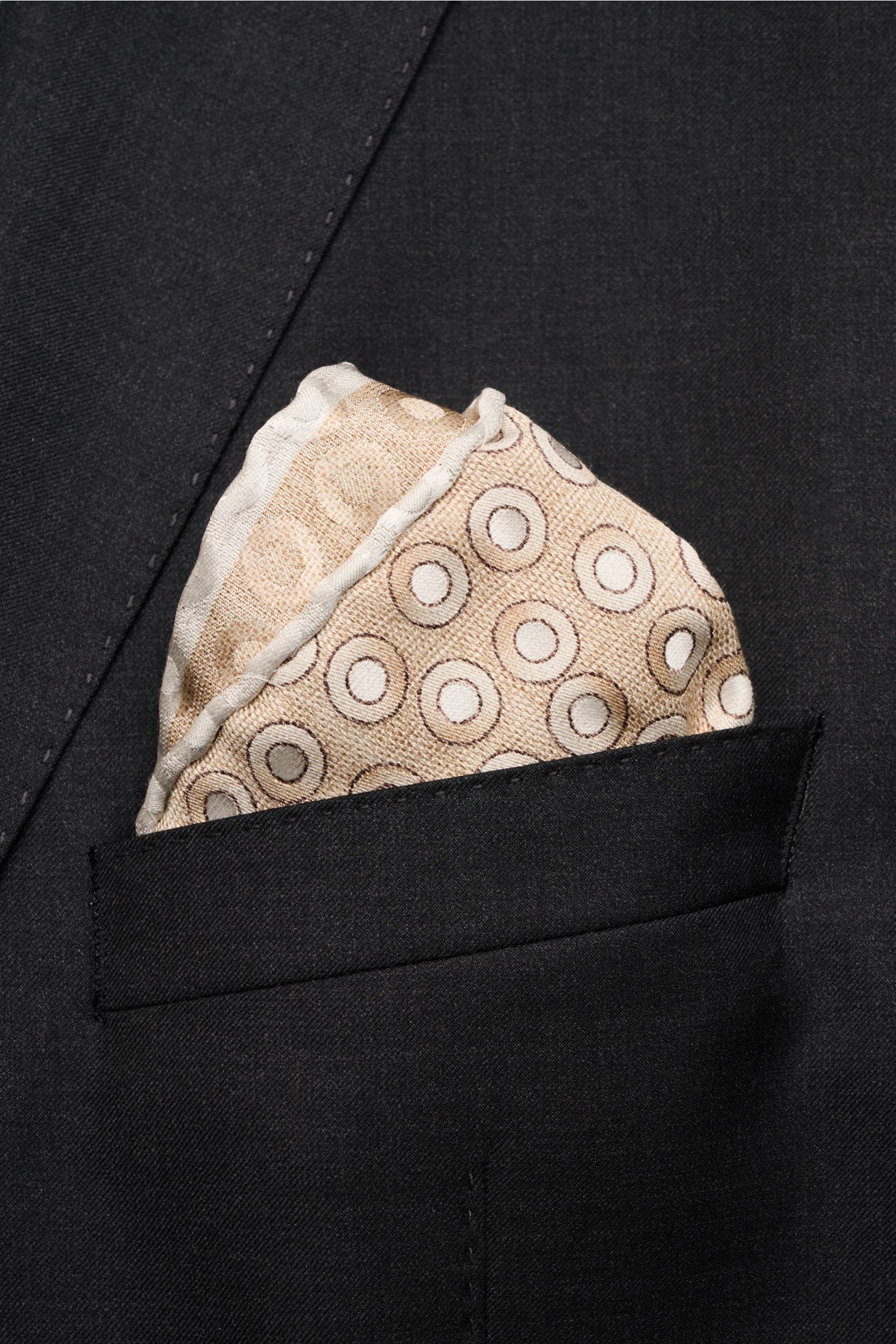 Brunello Cucinelli Seiden-Einstecktuch gold/hellgrau gepunktet shown from a close-up frontal view tucked into a black jacket pocket. Quiet Luxury heißt der große Trend: Das kann BRUNELLO CUCINELLI besonders gut und bringt auch in dieser Saison passende Ei