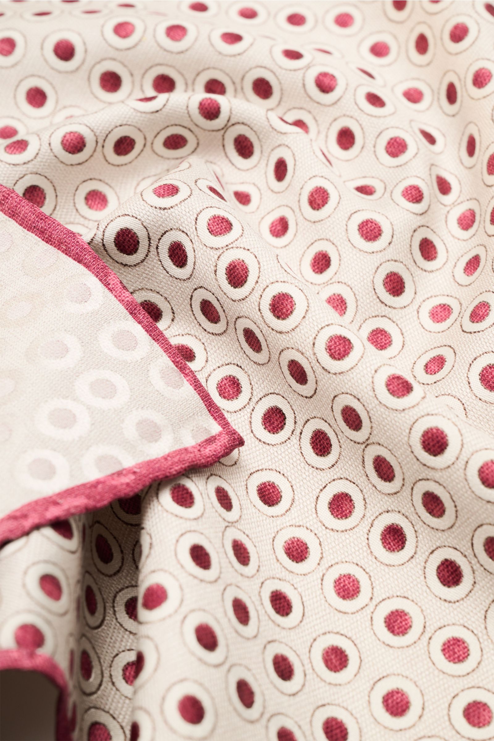 Close-up top-down view of Brunello Cucinelli Seiden-Einstecktuch dunkelrot/beige gepunktet silk pocket square with red-beige polka dots and handrolled edges.

Description: Quiet Luxury heißt der große Trend: Das kann BRUNELLO CUCINELLI besonders gut un