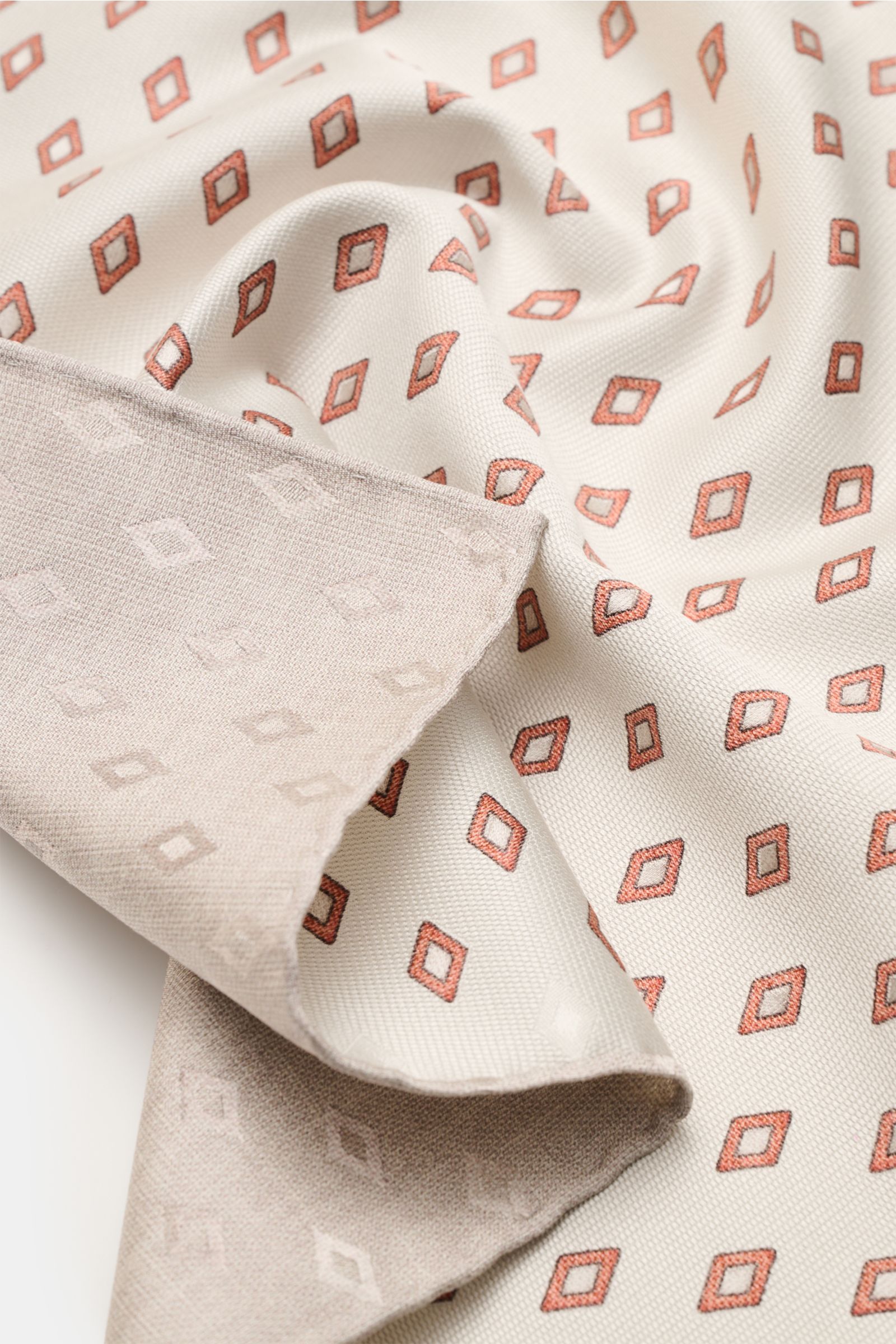 Brunello Cucinelli Seiden-Einstecktuch sand/rostbraun/beige gemustert shown close-up from above, highlighting its elegant diamond pattern, smooth pure silk texture, contrasting backside, and finely rolled edges in a contrasting color. Eleganter Akzent: