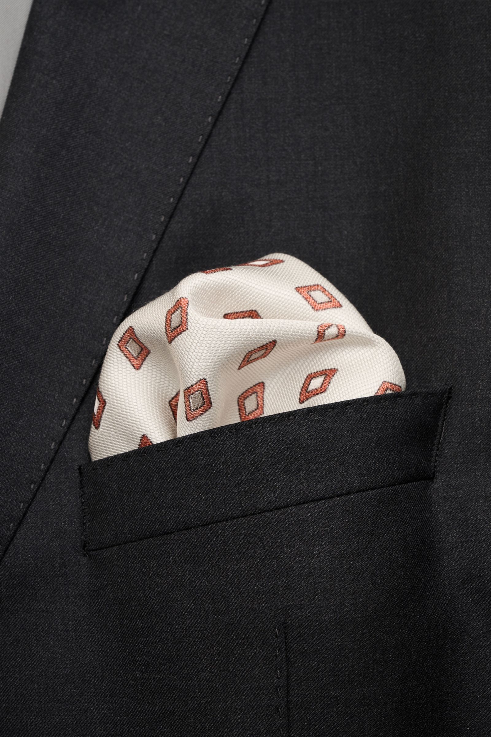 Brunello Cucinelli Seiden-Einstecktuch sand/rostbraun/beige gemustert, pure silk pocket square with elegant diamond pattern and rolled edges, shown from front close-up in a black jacket pocket. Eleganter Akzent: Das Einstecktuch aus reiner Seide von BR