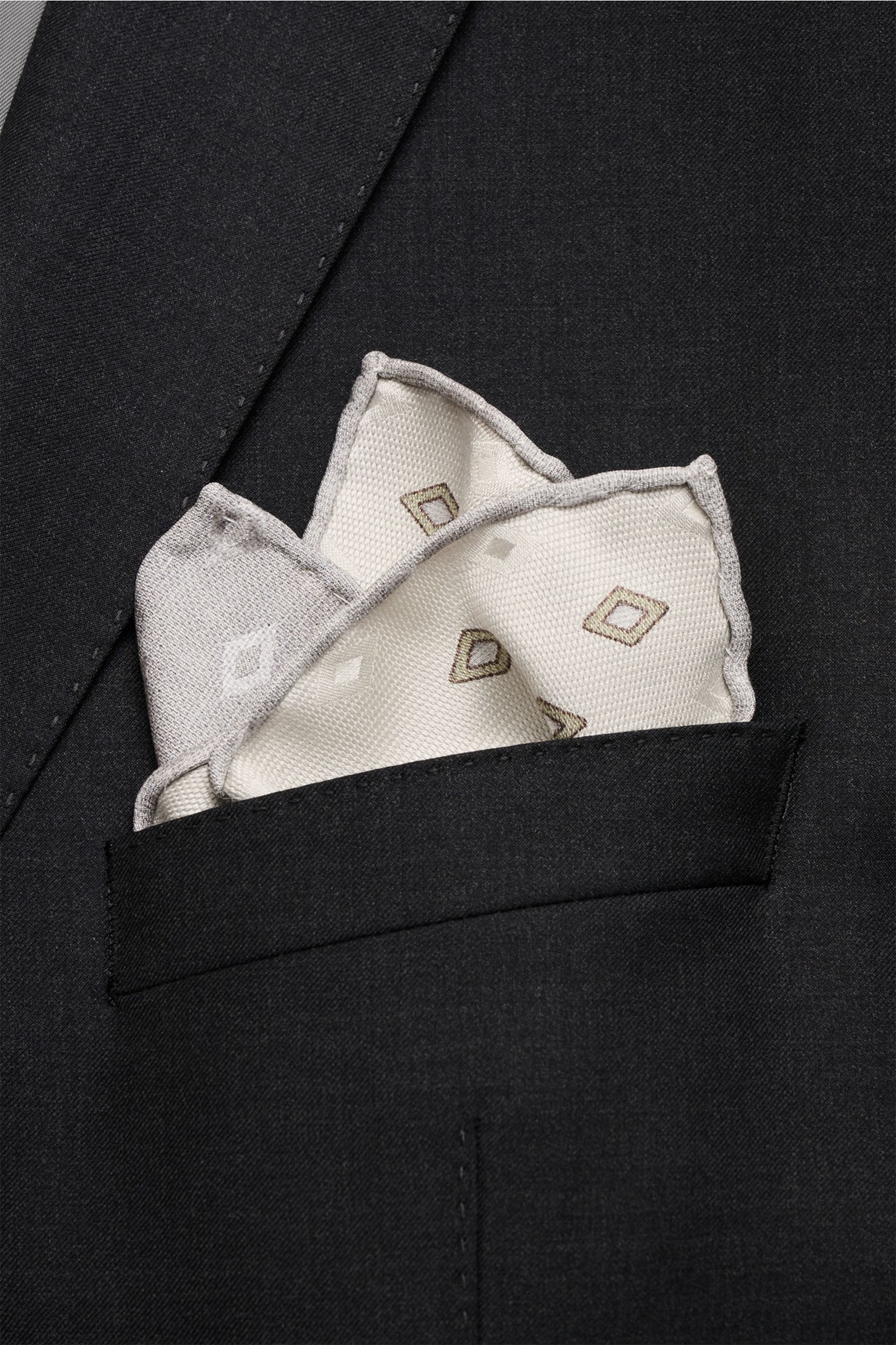 Brunello Cucinelli Seiden-Einstecktuch sand/salbei/grau gemustert, elegant silk pocket square with diamond pattern, rolled edges, photographed close-up from the front in a black suit pocket. Eleganter Akzent: Das Einstecktuch aus reiner Seide von BRUNE