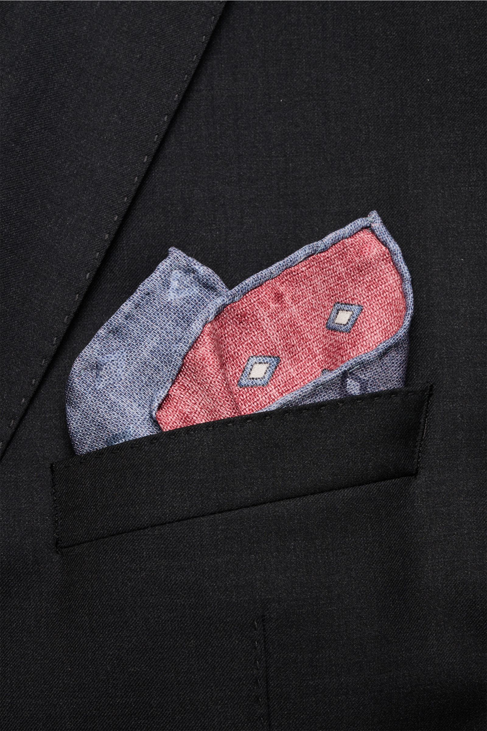 Close-up front view of Brunello Cucinelli Seiden-Einstecktuch rot/rauchblau/hellgrau gemustert in a black jacket pocket, showing its elegant diamond pattern, pure silk material, smooth texture, contrasting backside, and finely rolled edges in contrast col