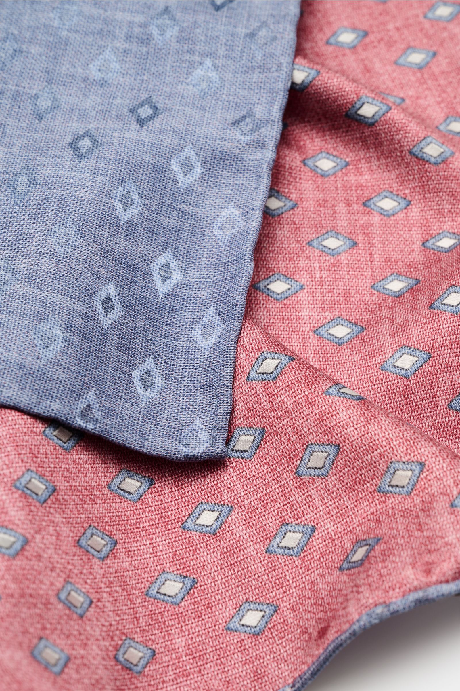 Close-up top view of the Brunello Cucinelli Seiden-Einstecktuch rot/rauchblau/hellgrau gemustert showing its elegant red silk with diamond pattern and contrasting blue backside with rolled edges. Eleganter Akzent: Das Einstecktuch aus reiner Seide von 