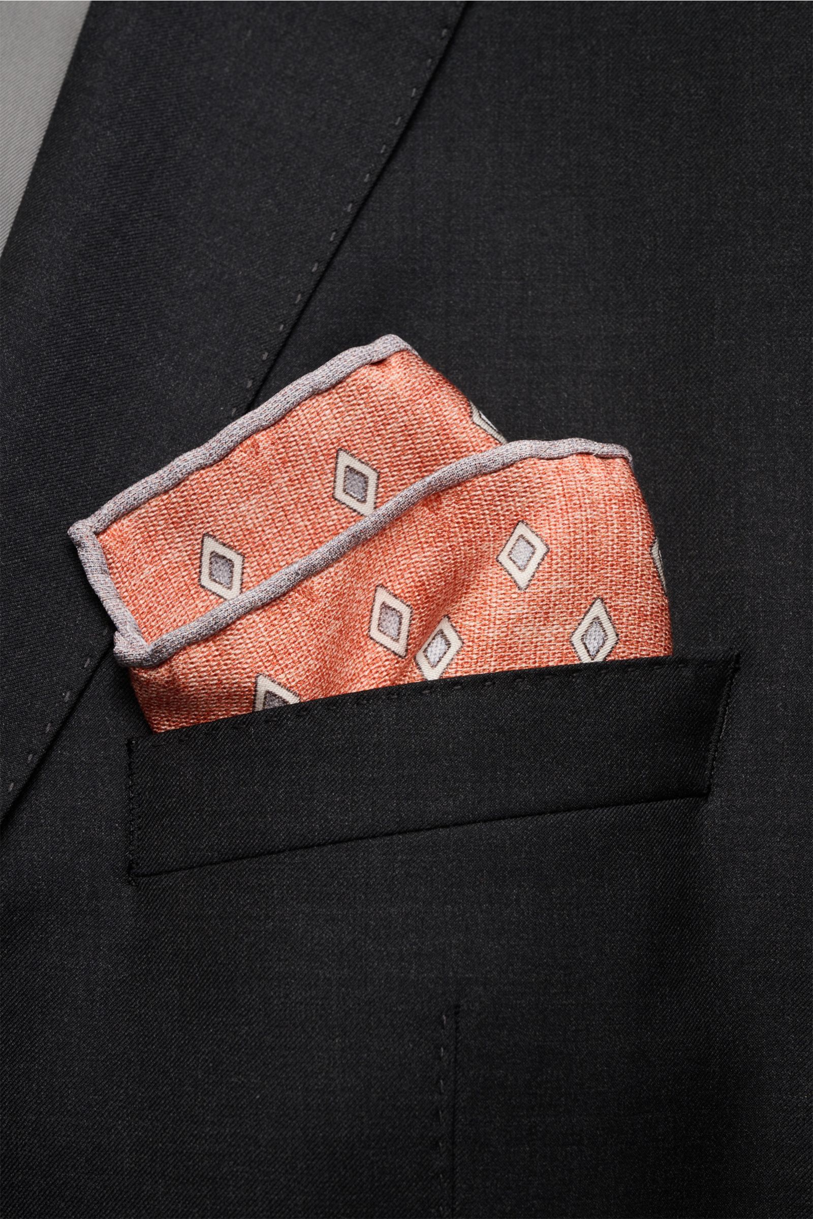 Brunello Cucinelli Seiden-Einstecktuch rostbraun/grau/hellgrau gemustert shown from a close-up front angle tucked in a black suit pocket. Eleganter Akzent: Das Einstecktuch aus reiner Seide von BRUNELLO CUCINELLI überzeugt mit seinem edlen Rautenmuster un