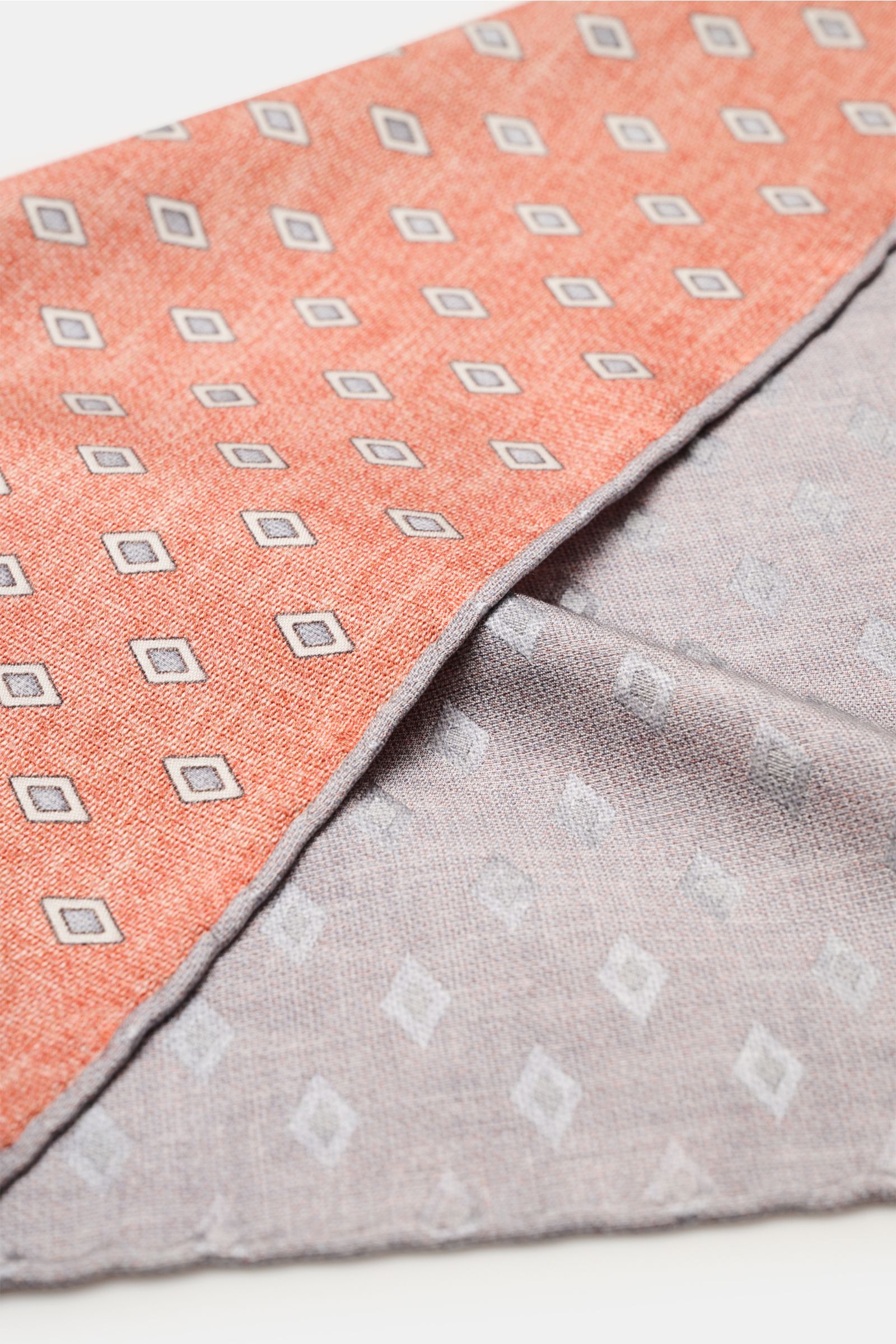 Brunello Cucinelli Seiden-Einstecktuch rostbraun/grau/hellgrau gemustert shown close-up from an angled top view, highlighting its elegant diamond pattern, smooth pure silk fabric, and finely rolled contrasting edges. Eleganter Akzent: Das Einstecktuch 