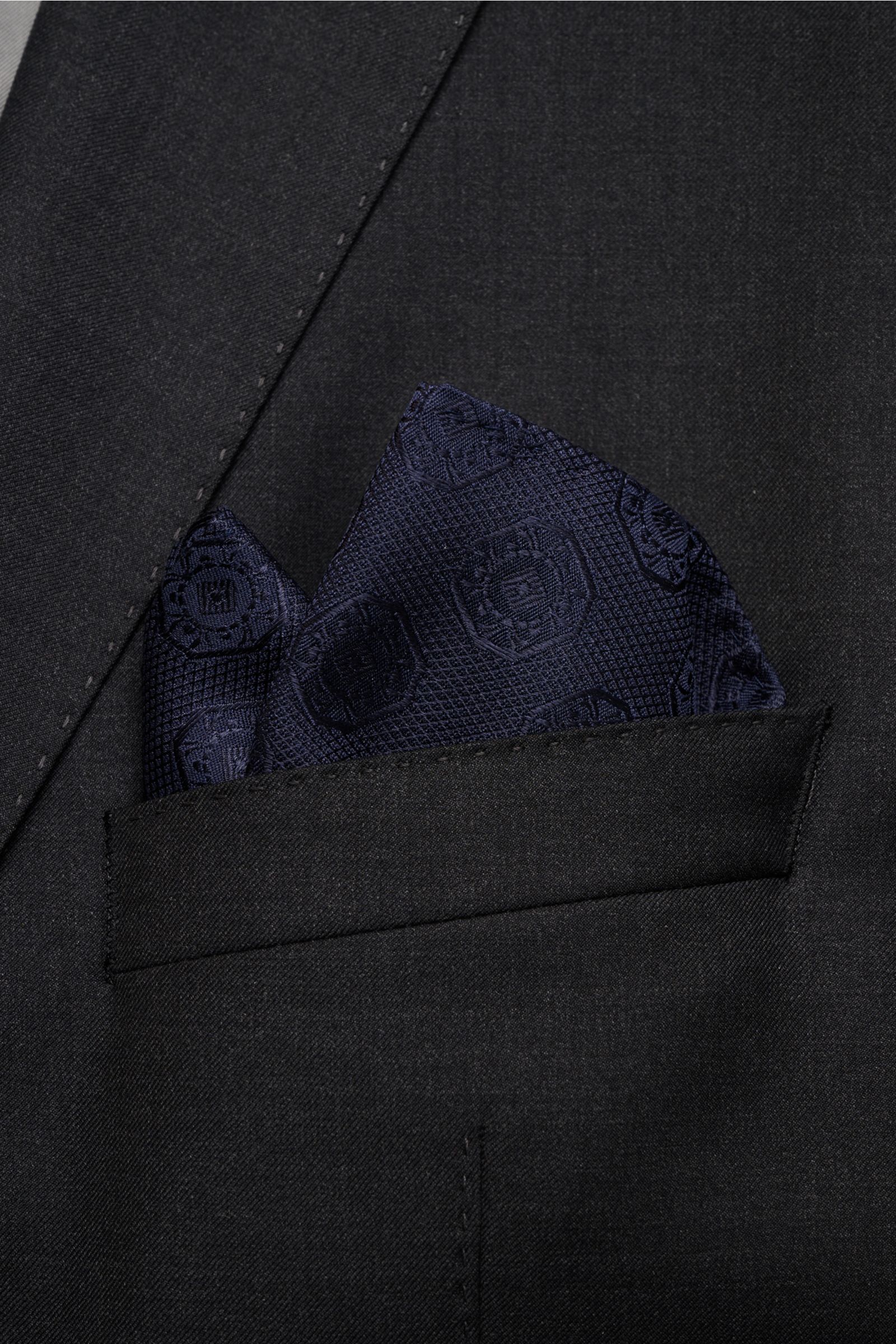 Close-up from above of a Brunello Cucinelli Silk pocket square dark navy, patterned, neatly folded in a black jacket pocket.

Elegant accent: This silk pocket square by BRUNELLO CUCINELLI has a fine medallion weave pattern that creates a subtle highlig