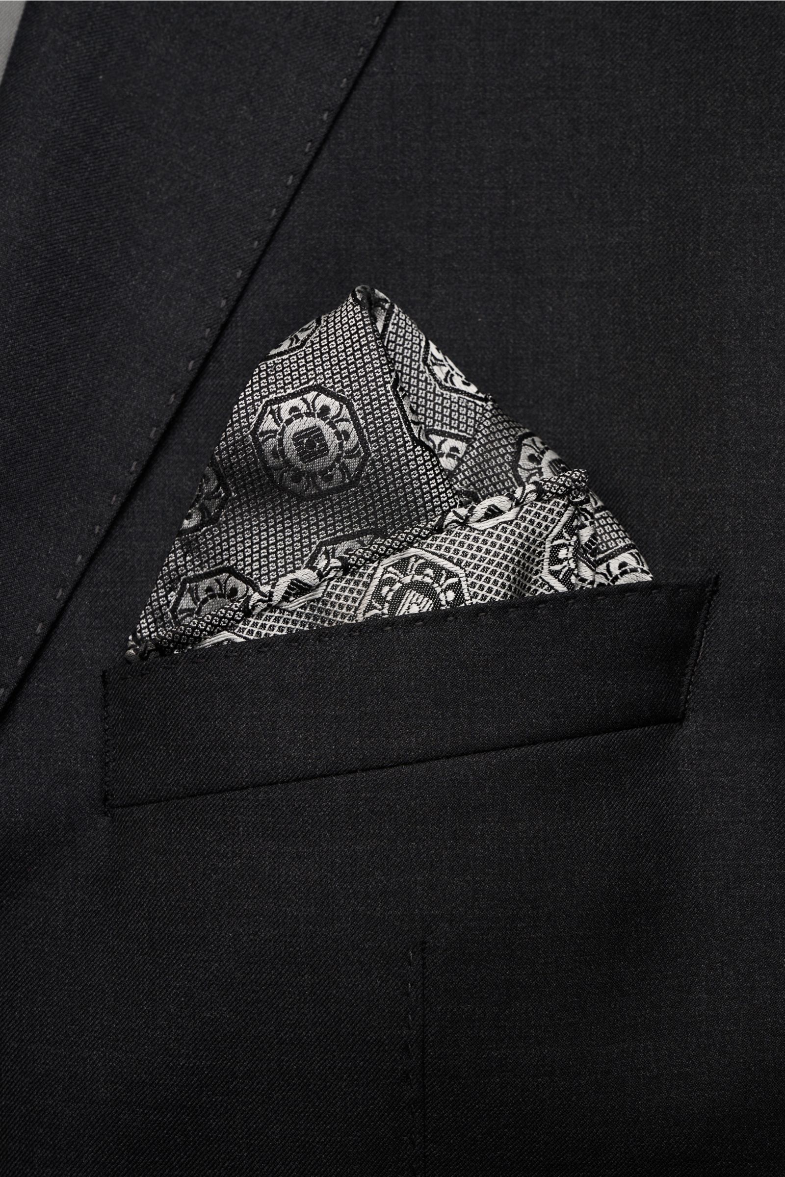 Brunello Cucinelli Silk pocket square grey/black patterned folded in a black jacket breast pocket, close-up front view.

Elegant accent: This silk pocket square by BRUNELLO CUCINELLI has a fine medallion weave pattern that creates a subtle highlight an