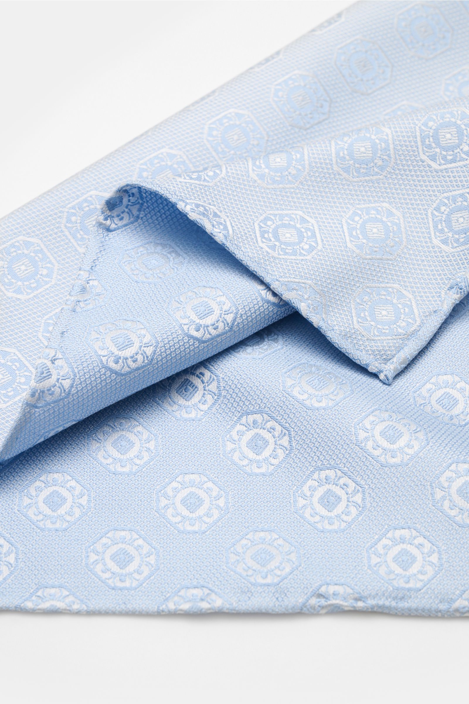 Close-up top-down view of a light blue/light grey patterned Brunello Cucinelli Silk pocket square with medallion weave.

Elegant accent: This silk pocket square by BRUNELLO CUCINELLI has a fine medallion weave pattern that creates a subtle highlight an