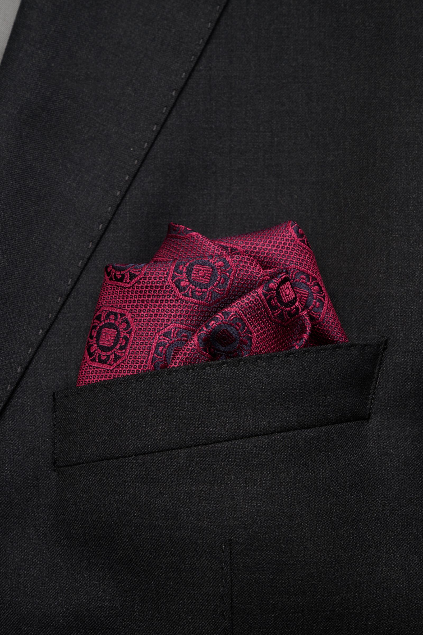 Close-up front view of a burgundy and dark navy patterned Brunello Cucinelli silk pocket square neatly folded in a black jacket pocket.

Description: Elegant accent: This silk pocket square by BRUNELLO CUCINELLI has a fine medallion weave pattern that 