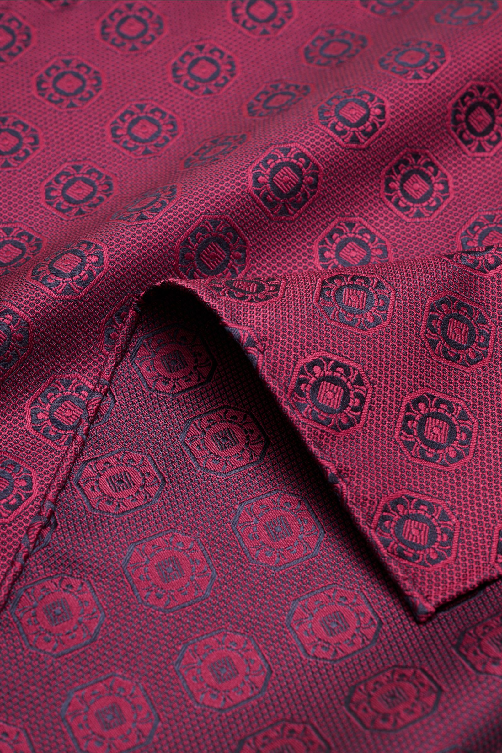 Alt tag (125 characters):
Close-up top-down view of Brunello Cucinelli Silk pocket square burgundy/dark navy patterned with medallion weave and rolled edges.

Additional description:
Elegant accent: This silk pocket square by BRUNELLO CUCINELLI has a f