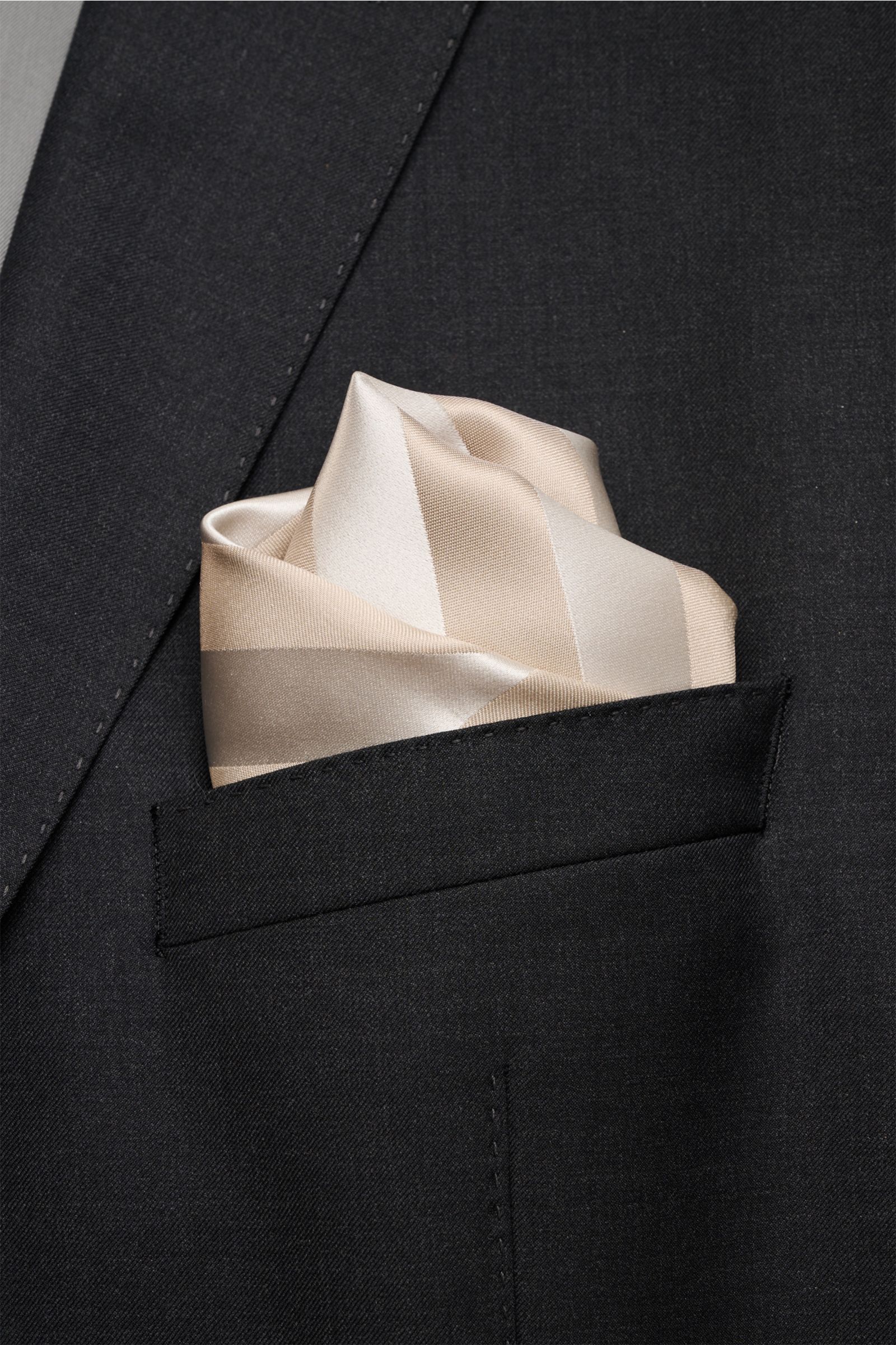 Brunello Cucinelli Seiden-Einstecktuch beige/creme gestreift in Brusttasche, glatter Griff, edles Streifenmuster, rollierte Kanten, reine Seide, Made in Italy, ca. 33x33 cm, Nahaufnahme frontal.