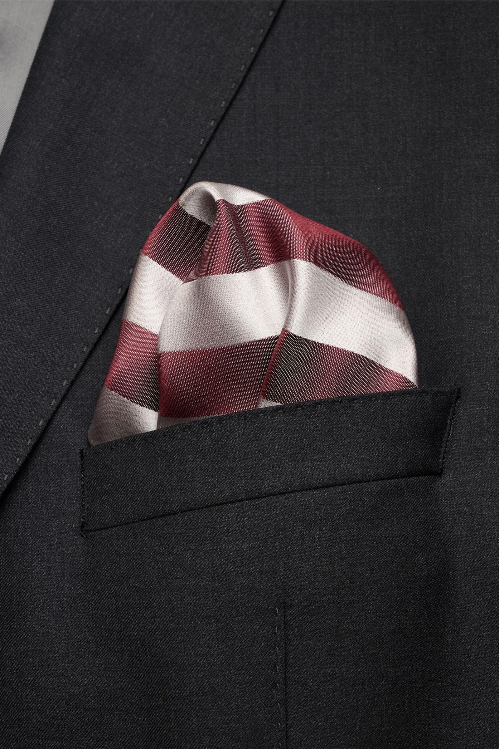 Brunello Cucinelli Seiden-Einstecktuch bordeaux/silbergrau gestreift aus reiner Seide mit edlem Streifenmuster, glattem Griff und rollierten Kanten, fotografiert in Nahaufnahme aus seitlicher Perspektive in der Brusttasche eines dunklen Sakkos.