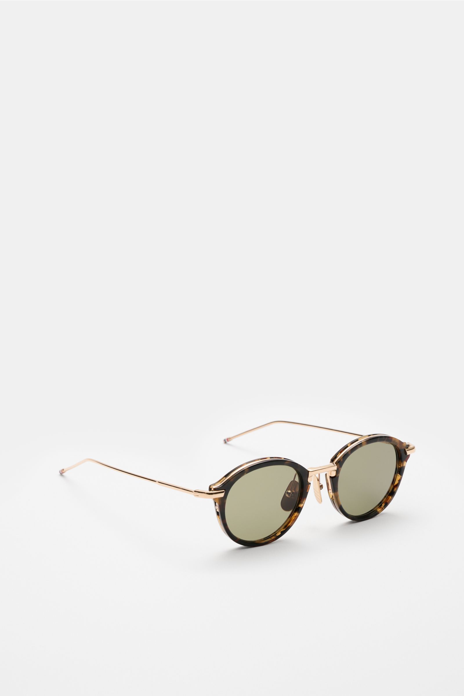 Thom Browne Sunglasses dark brown/gold patterned shown from a front-side angle, round tortoiseshell acetate frame, metal temples, tinted lenses with 100% UV protection, tricolour temple detail, hard case included.