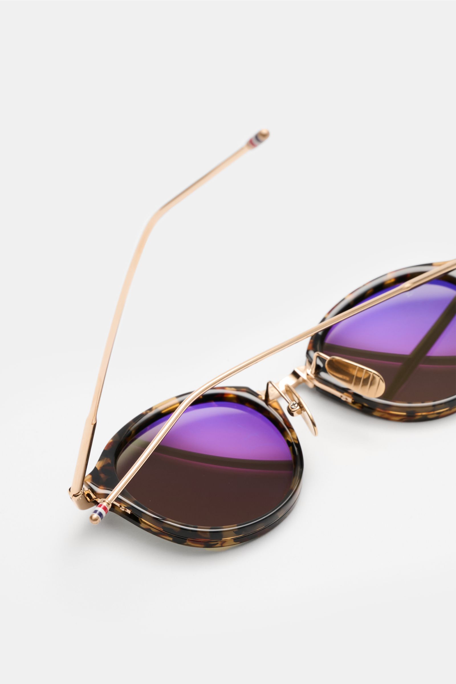 Thom Browne Sunglasses dark brown/gold patterned shown from a close-up rear angle, highlighting the tortoiseshell acetate frame with rounded shape, gold metal arms, tricolour temple detail, and slightly tinted plastic lenses offering 100% UV protection.

