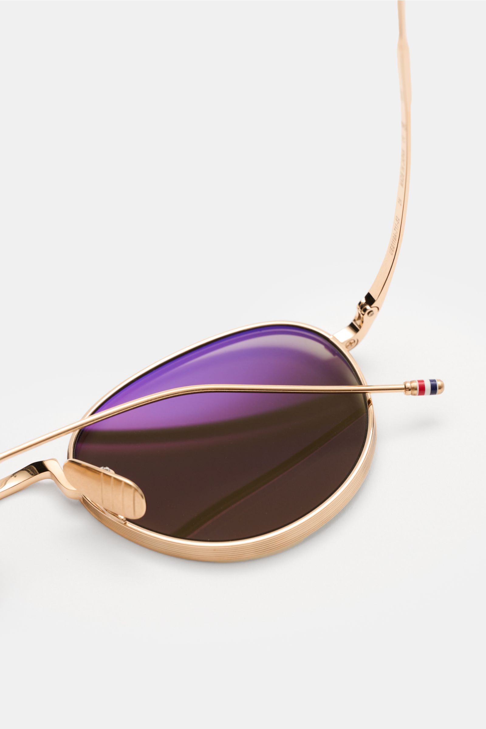 Nahaufnahme der Thom Browne Sonnenbrille gold, abgerundete Form mit tiefem Metallrahmen, gleichmäßig getönte Gläser und Tricolore-Detail am Bügel.
