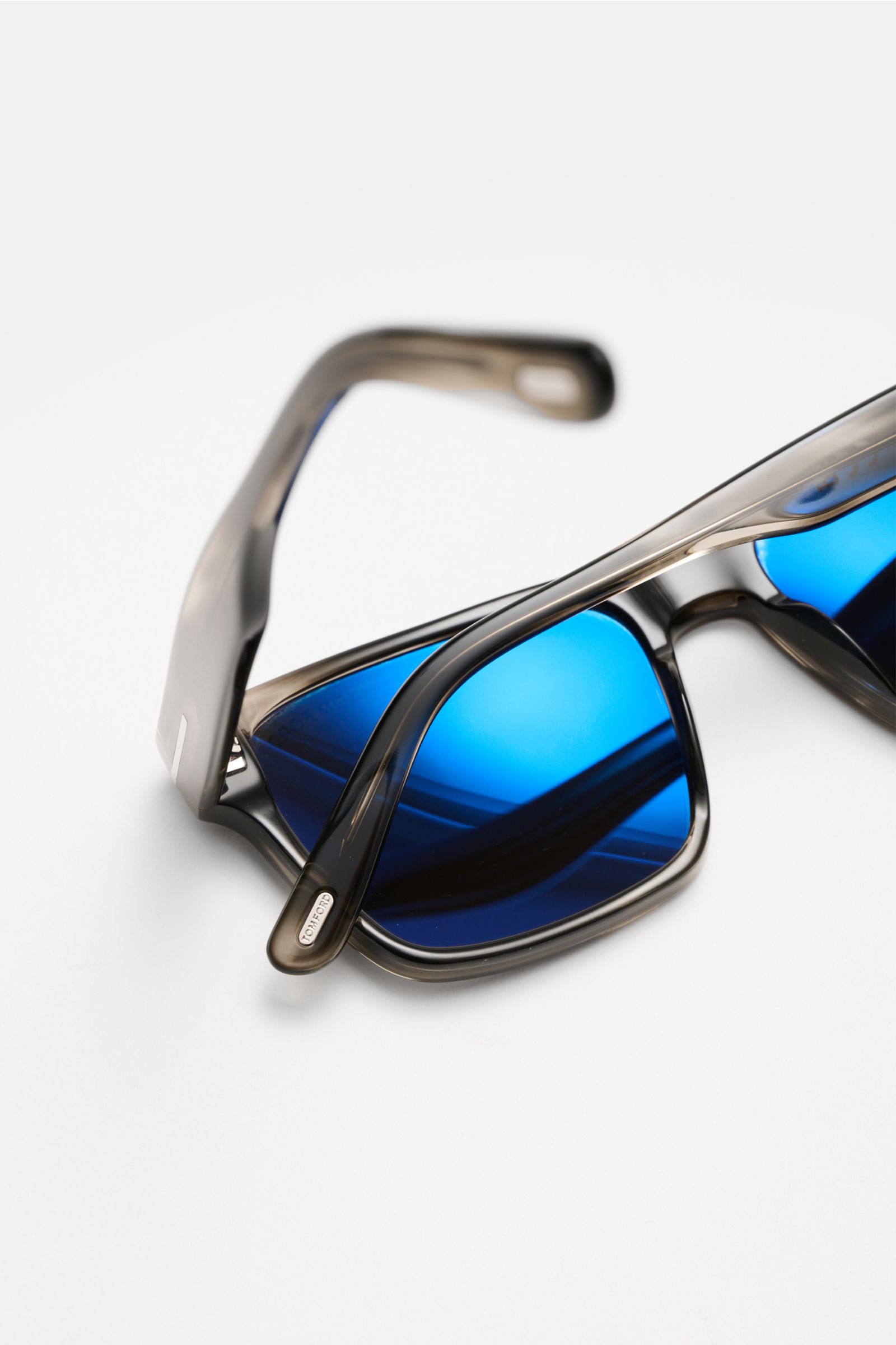 Close-up of Tom Ford Sunglasses 'Calder' grey folded on a white surface, showing square shape, polarised blue lenses, and acetate frame from an angled top view.

Stylish all-rounder: With their timeless design, these sunglasses by TOM FORD are an ideal