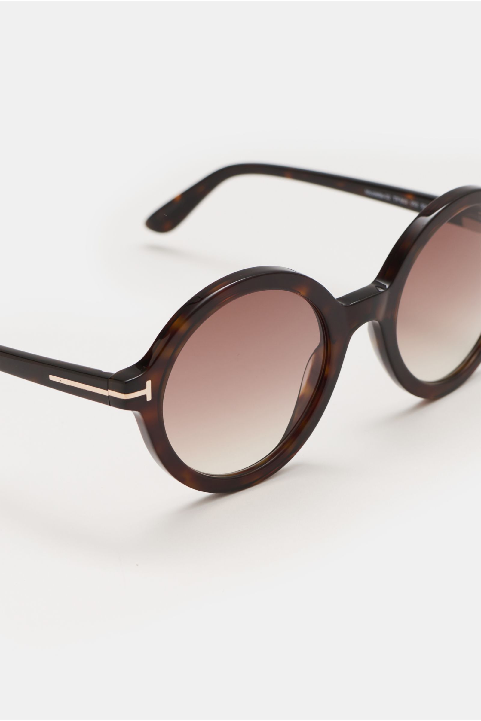 Close-up side-angle view of Tom Ford Sunglasses 'Nicolet' dark brown patterned with round tortoiseshell acetate frame, evenly tinted lenses, and signature ‘T’ detail on the temple. The 'Nicolette' sunglasses from TOM FORD impress with their eye-catchin