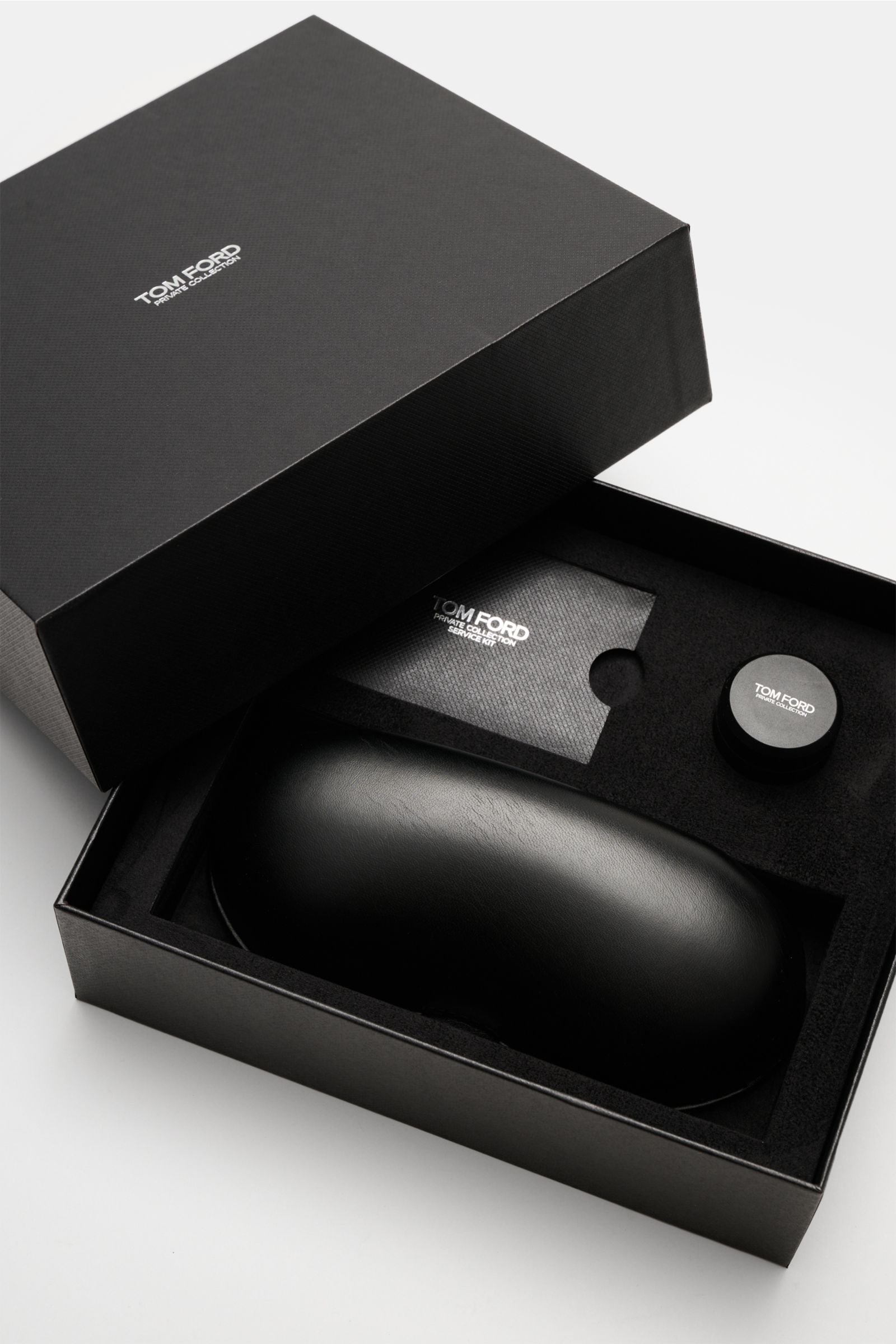 Open black Tom Ford box shown from a top front angle, containing a sleek leather hard case, a service kit, and a horn polish set for the Tom Ford Horn-Sonnenbrille 'Private Collection' schwarz/grau/sand gemustert. The luxurious 'Private Collection' by TOM